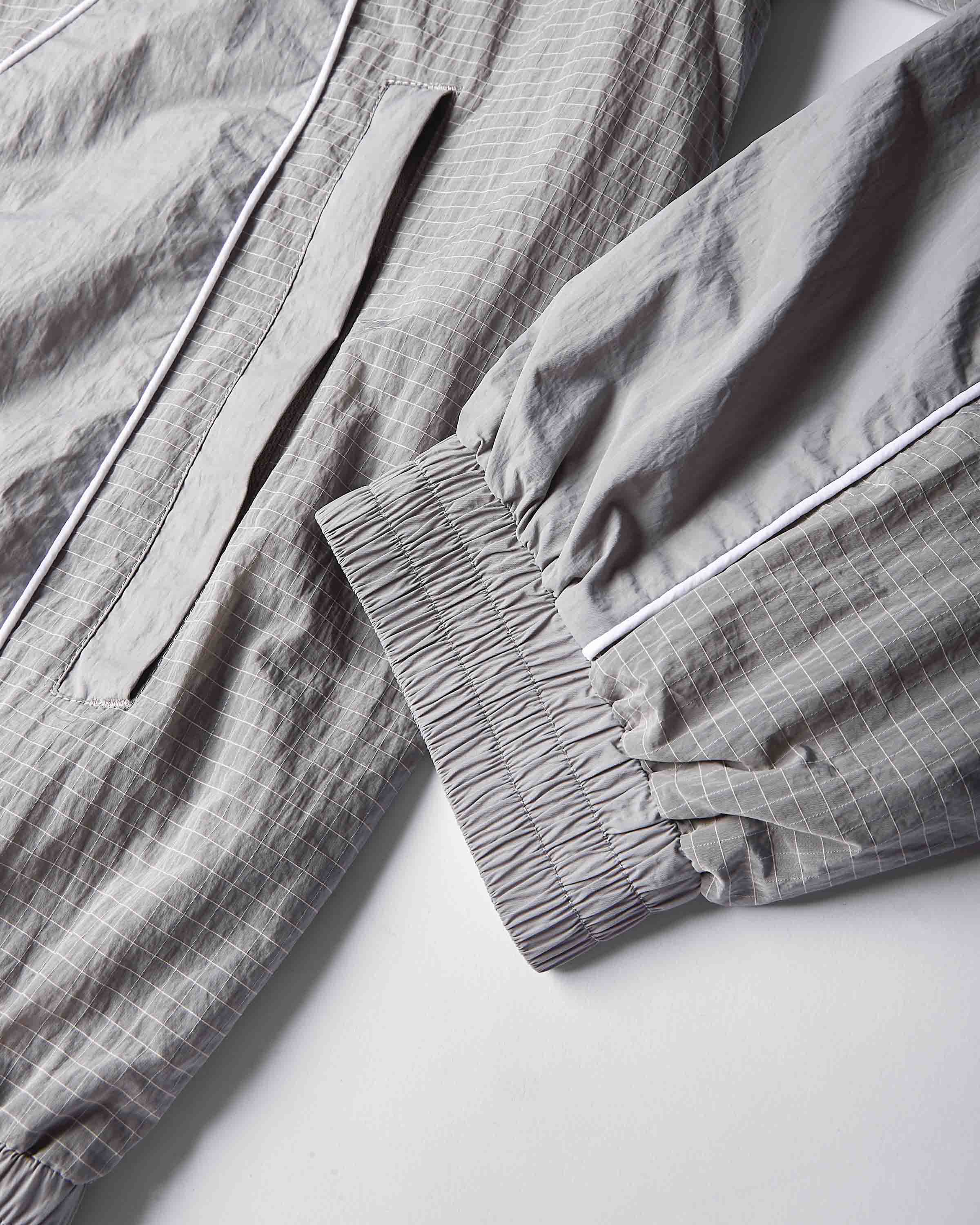 Close-up of a light gray and white checkered lounge set, showing the elasticized cuff of one sleeve and a matching drawstring detail on the other piece.