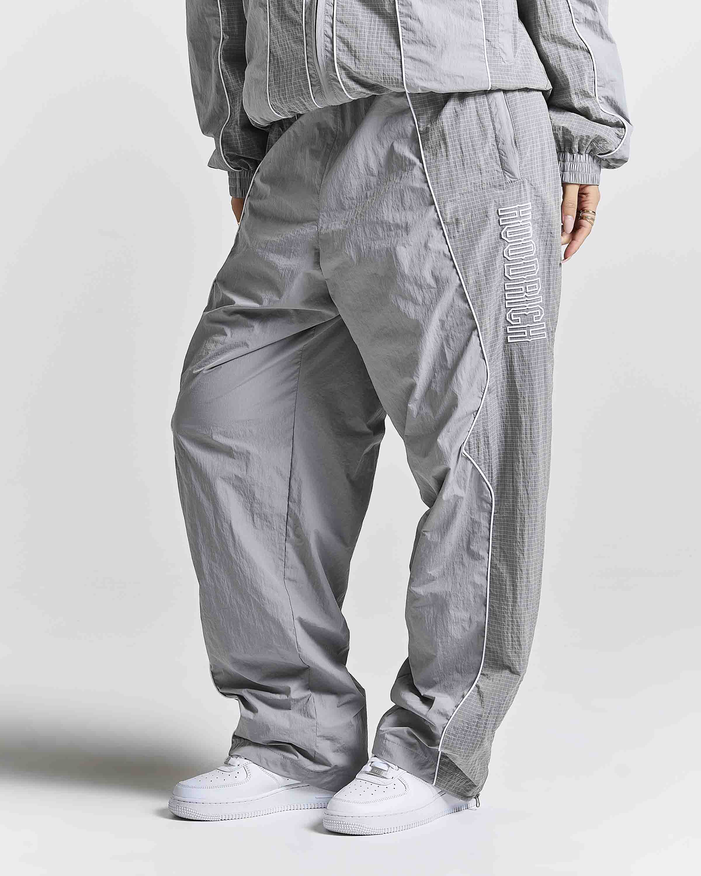 A person wearing loose-fit gray pants with a subtle grid texture, white sneakers, and a matching gray jacket against a light gray studio background.