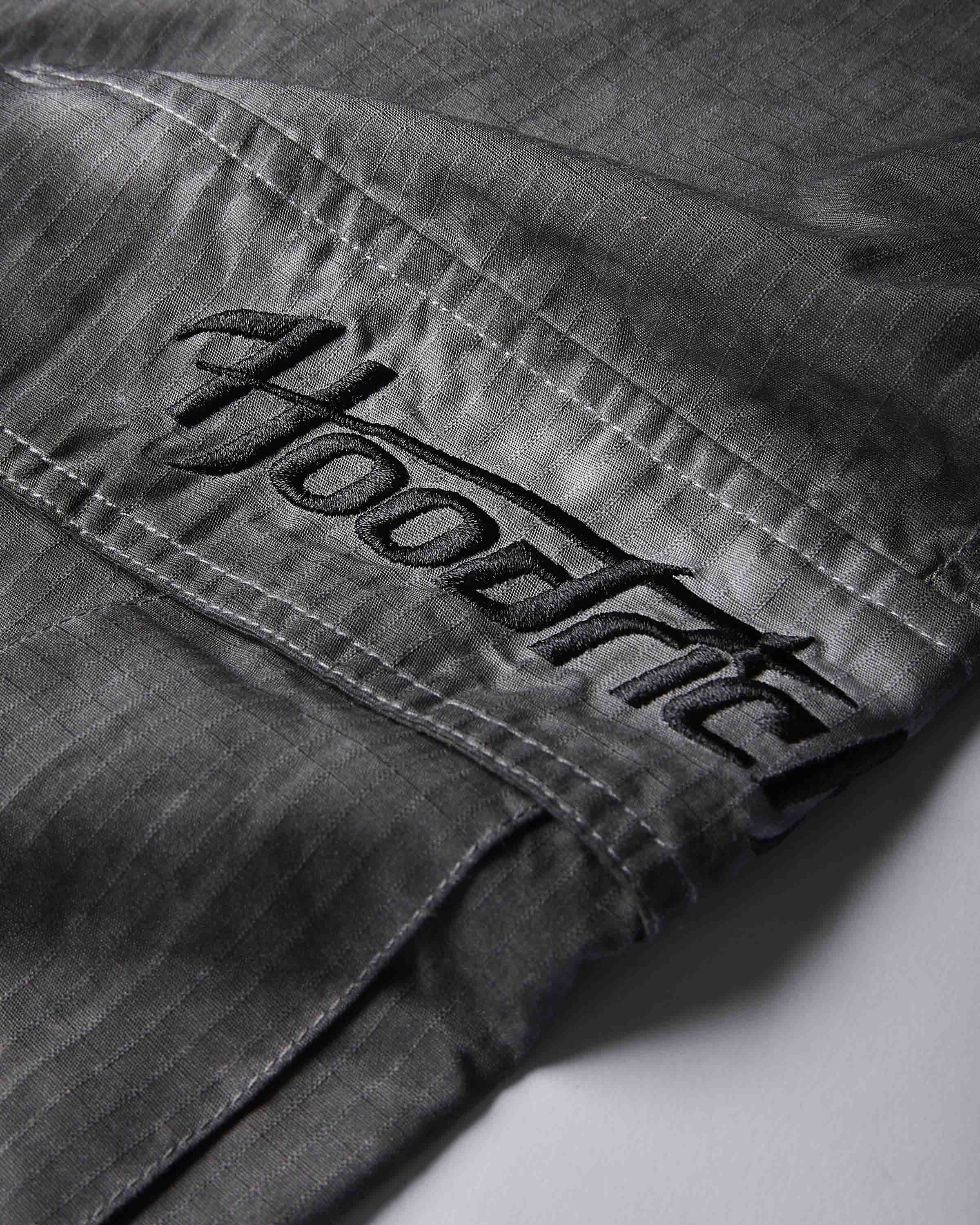 Close-up of dark gray denim fabric with a large embroidered black 'Hoodrich' logo patch on the pocket.