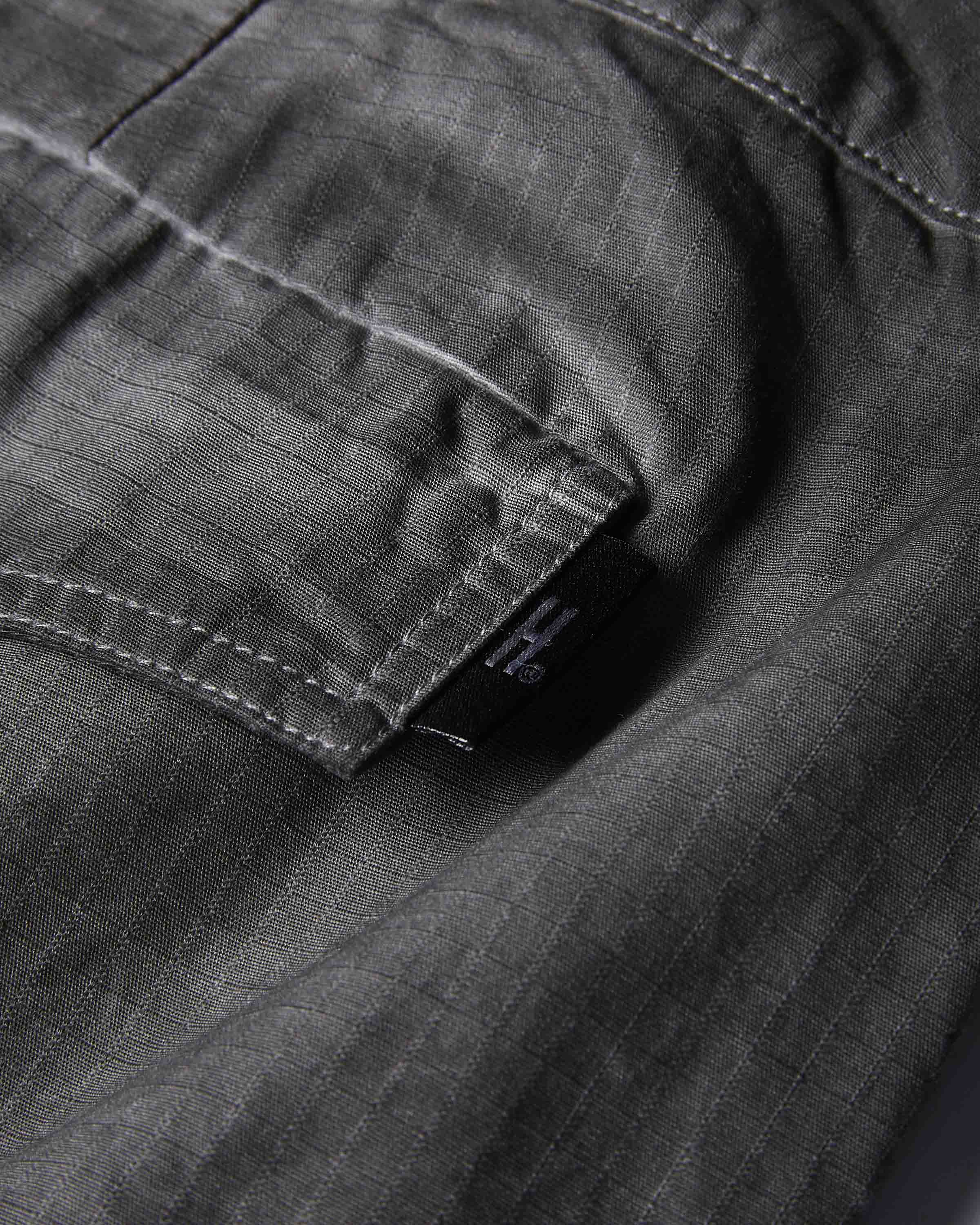 Close-up of dark gray textured fabric with a pocket and a small black brand tab showing the stylized H logo.