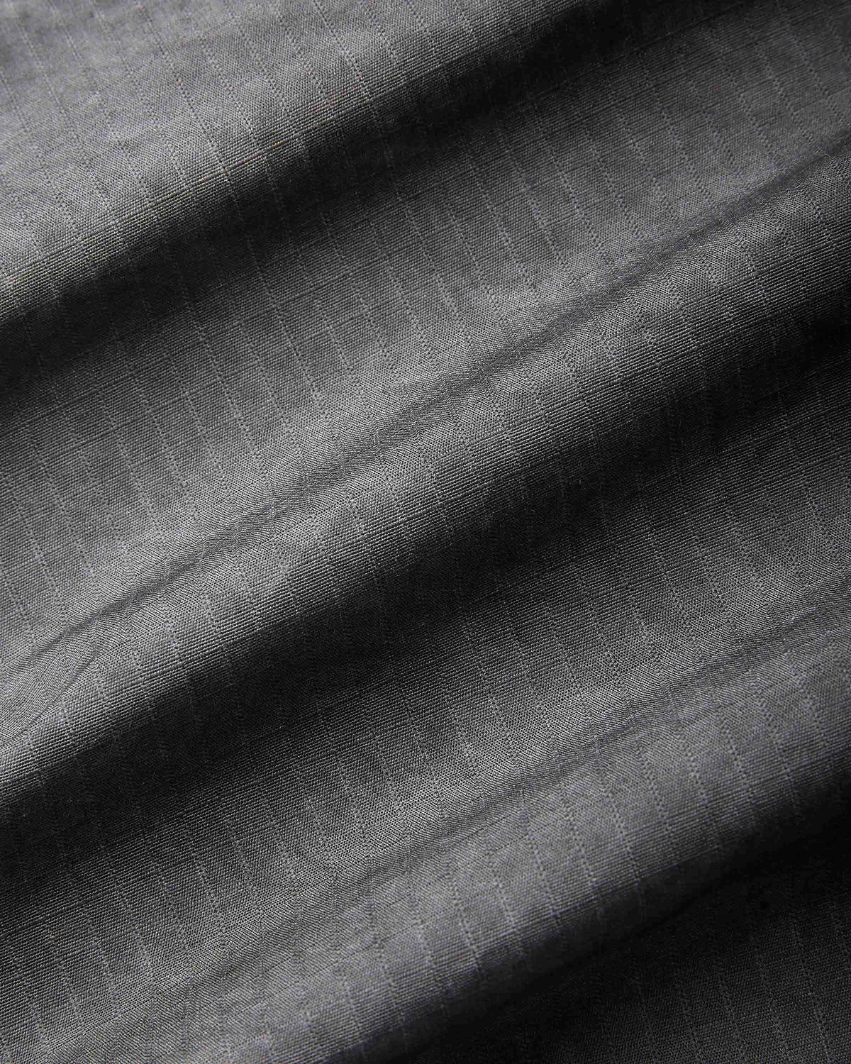 A close-up of dark gray textured fabric with a subtle woven grid pattern and soft diagonal folds.