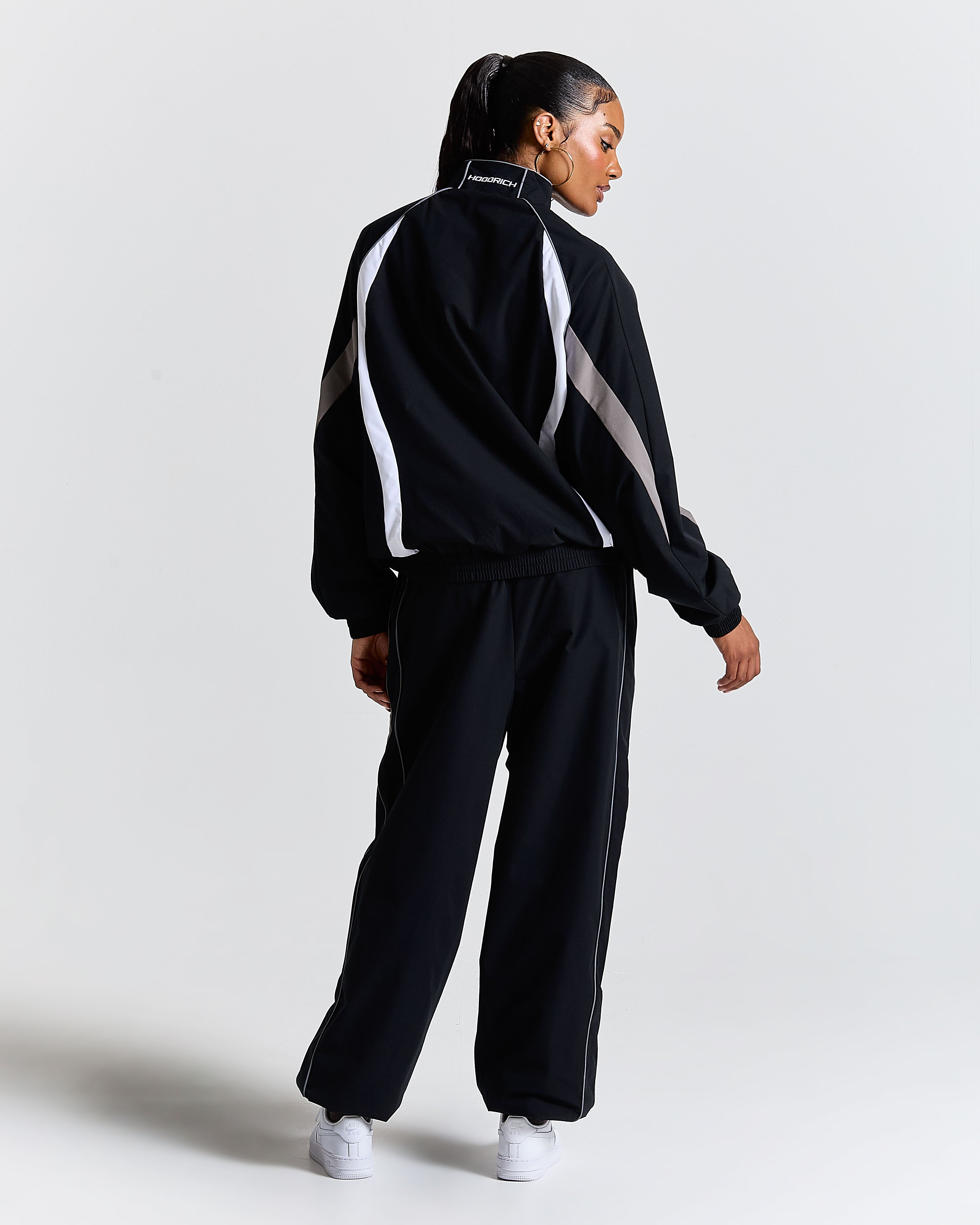Person wearing a black tracksuit with white stripes on a light gray background