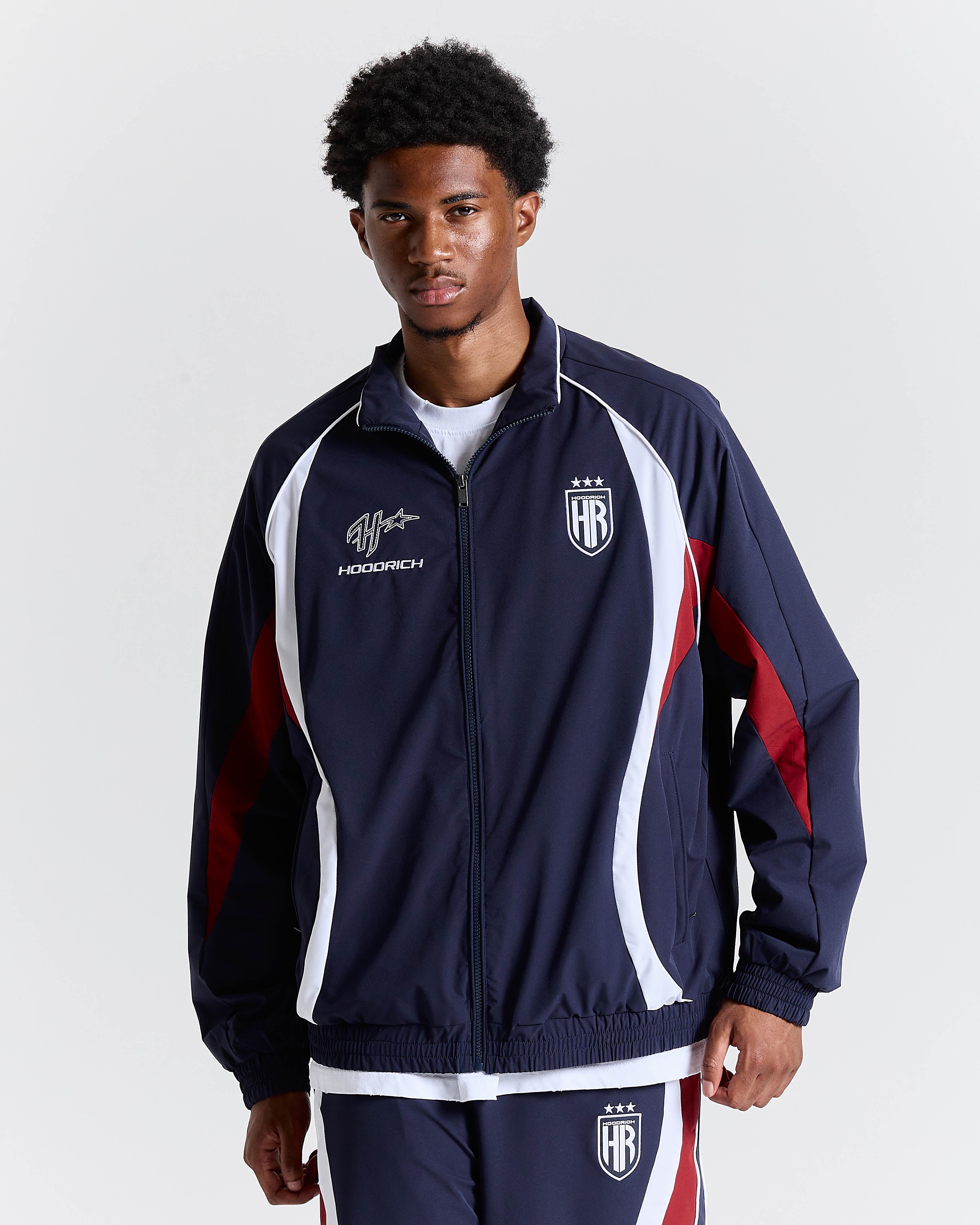 Person wearing a navy tracksuit with red and white accents on a light gray background