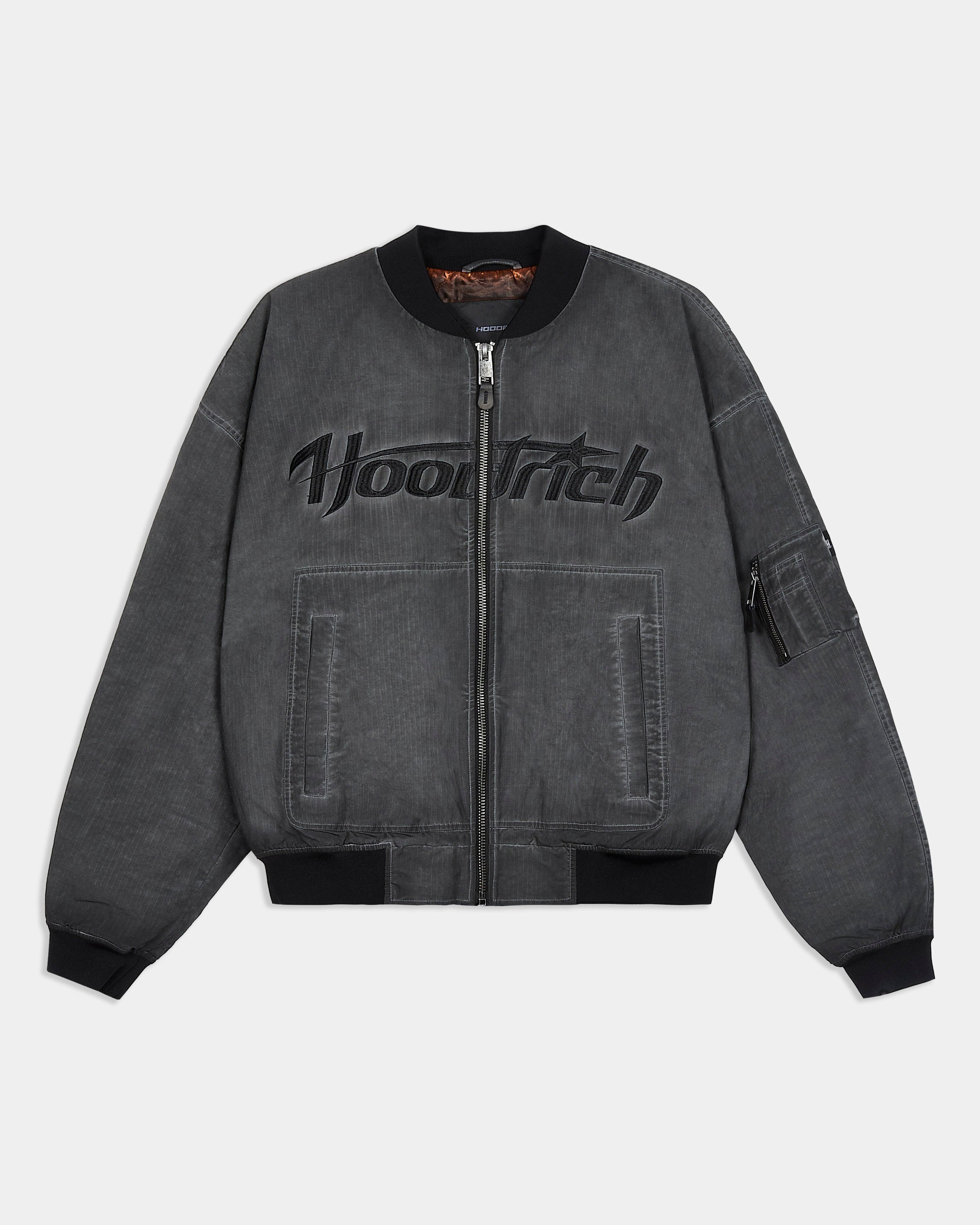A dark gray washed bomber jacket with a black embroidered 'Hoodrich' logo across the chest, featuring a front zipper, ribbed collar, cuffs, and hem, and zippered side pockets.