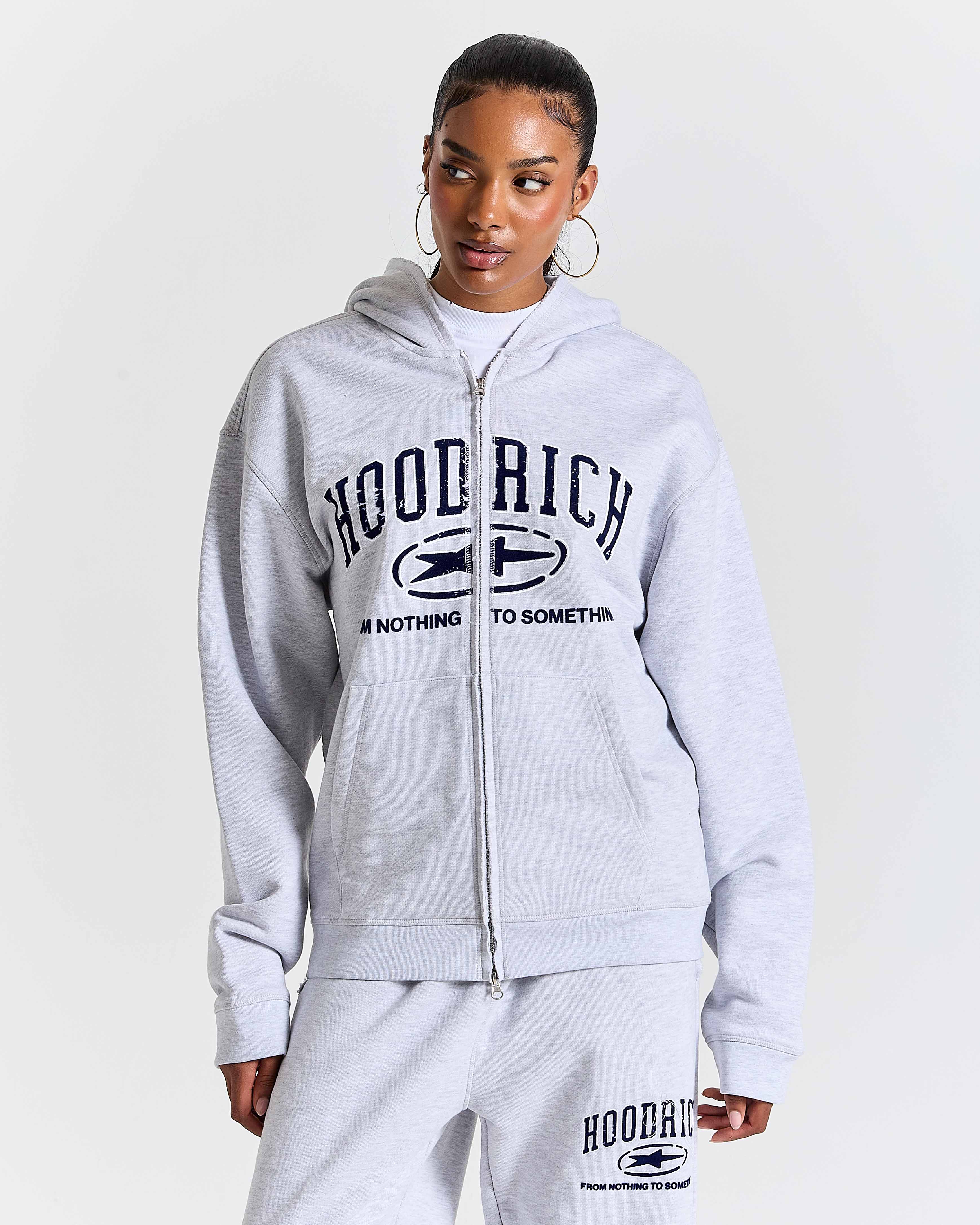 Person wearing a gray 'Hoodrich' tracksuit on a white background