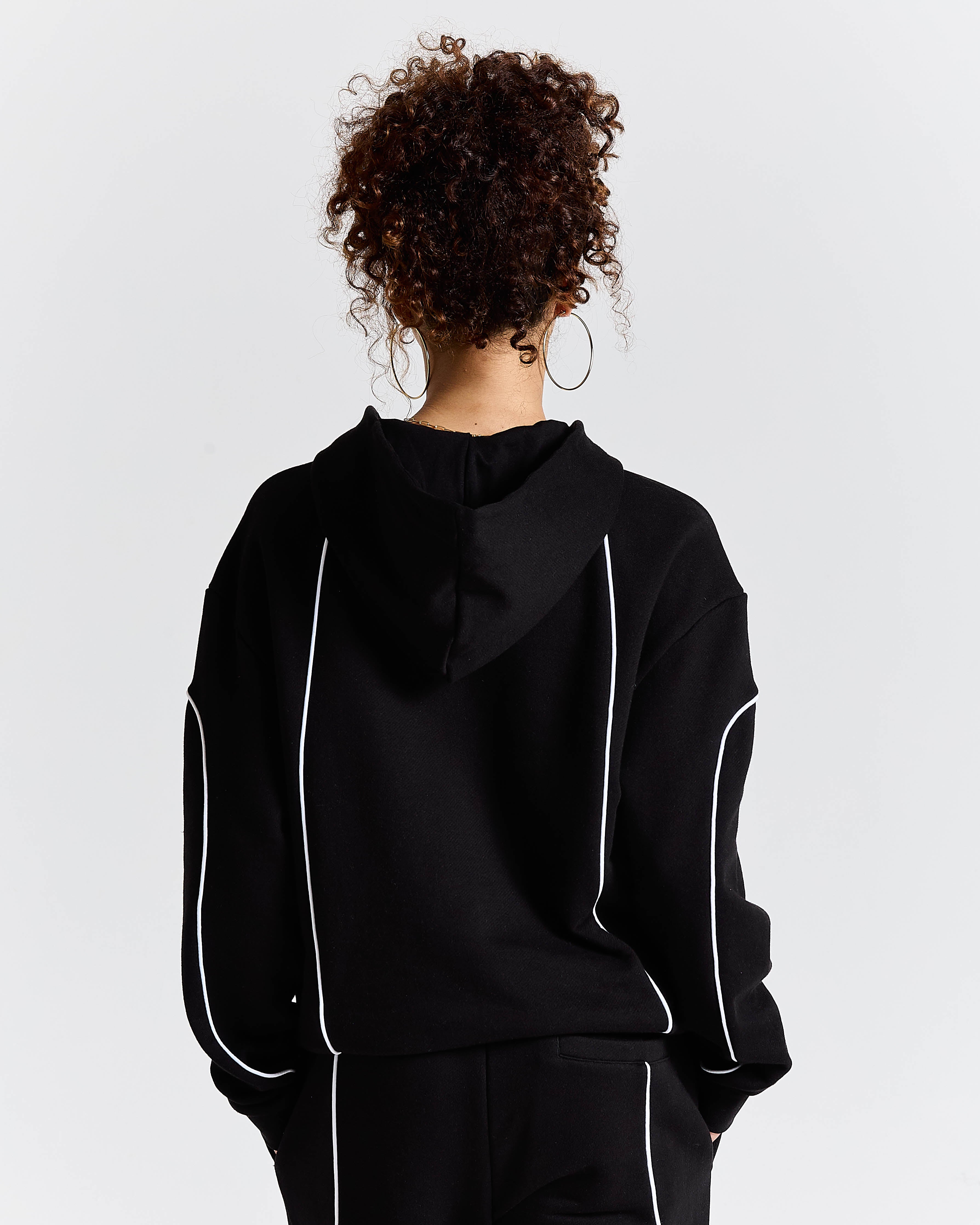 Person wearing a black hoodie with white accents on a plain background