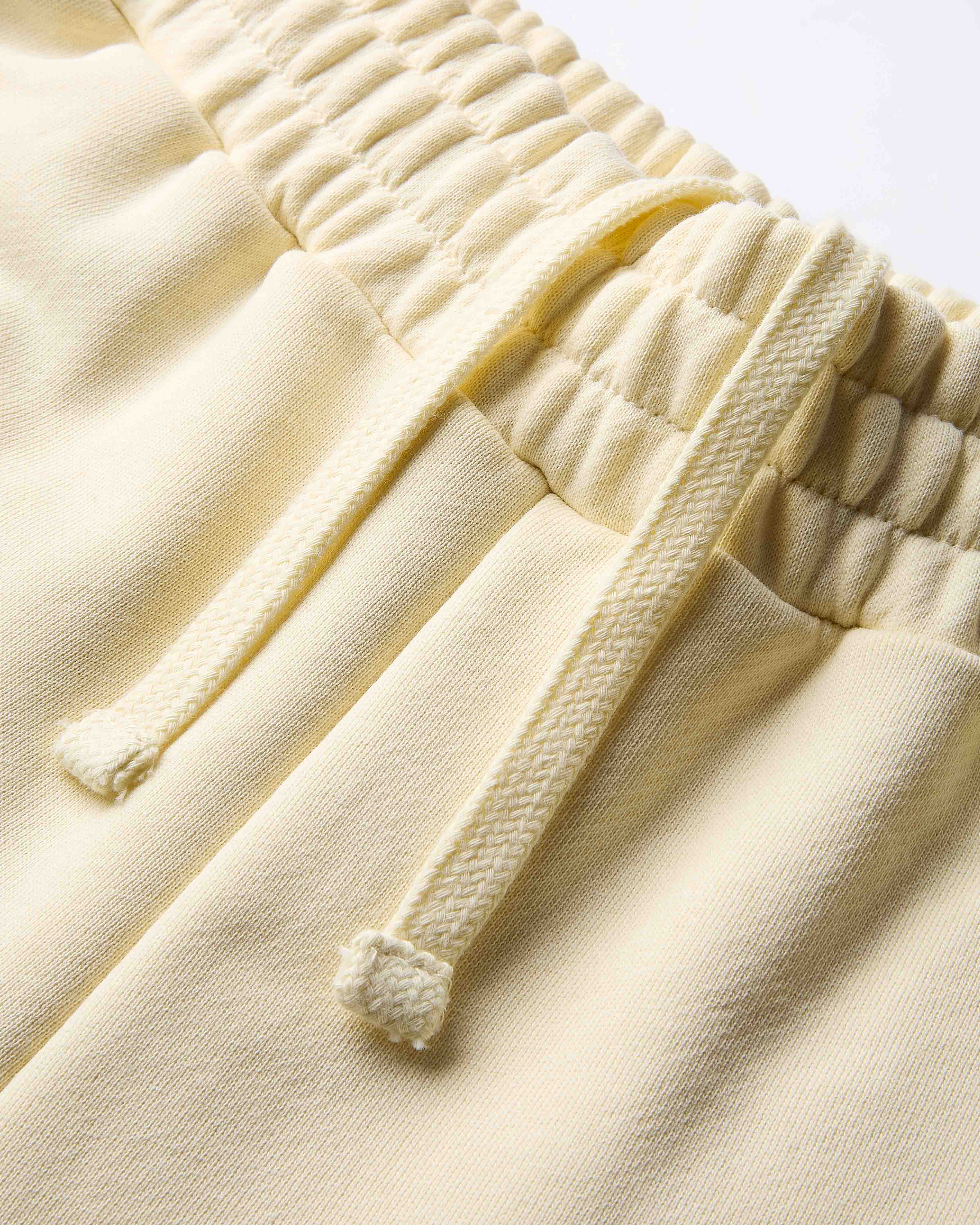 Close-up of cream-colored pants with textured drawstring waistband on a light background