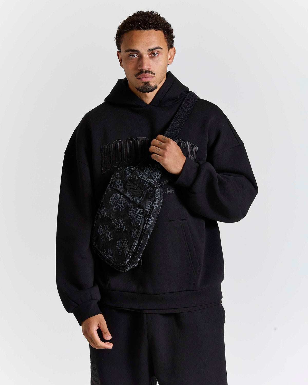 Displays a model wearing the Black & Grey 'Hoodrich' Virtux Sling Bag