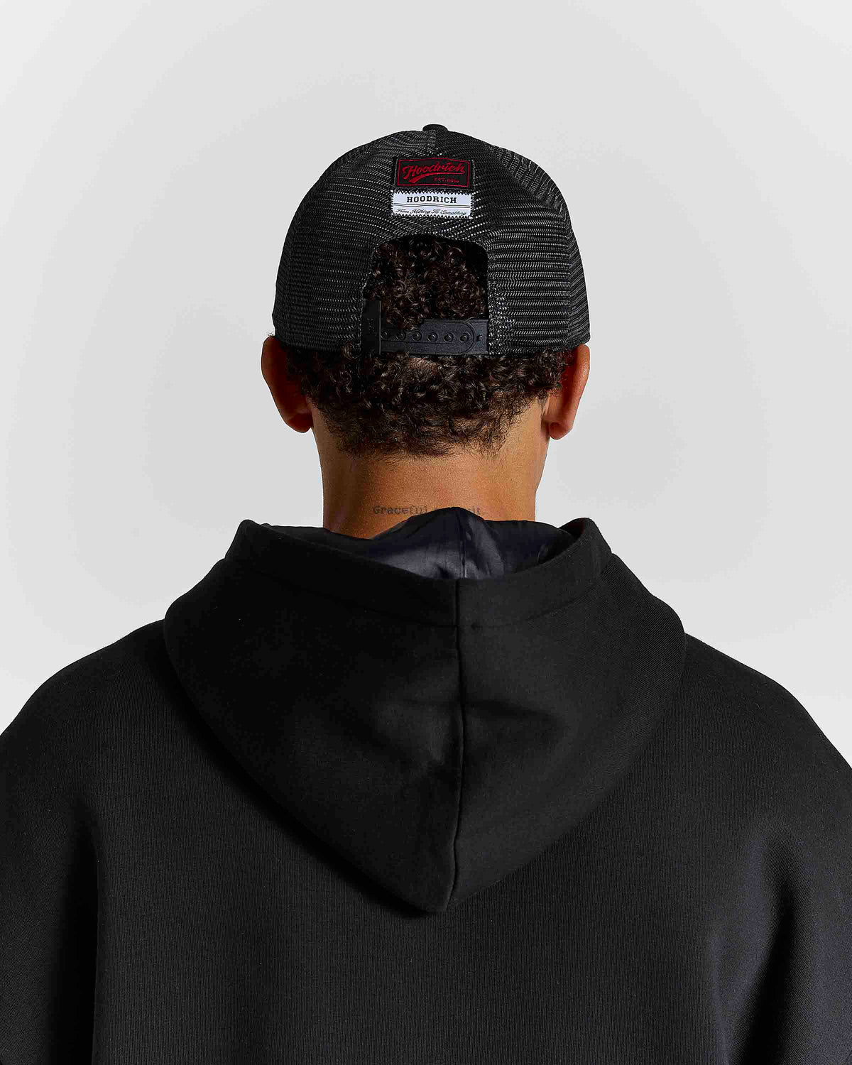 Displays a model wearing the black 'hoodrich' branded Stade 5 Panel Cap