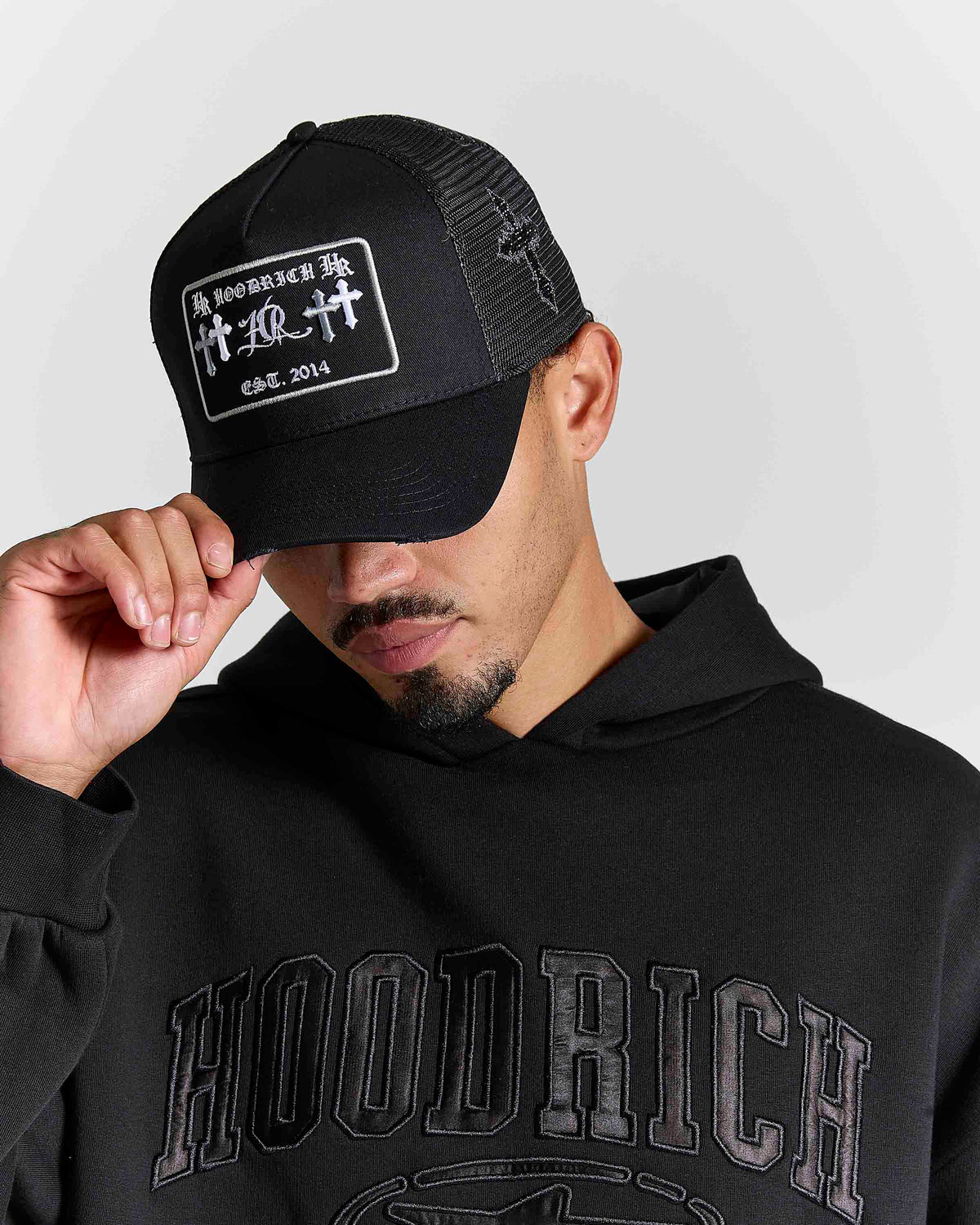 Displays a model wearing the black & grey 'Hoodrich' branded Nocturn Trucker Cap