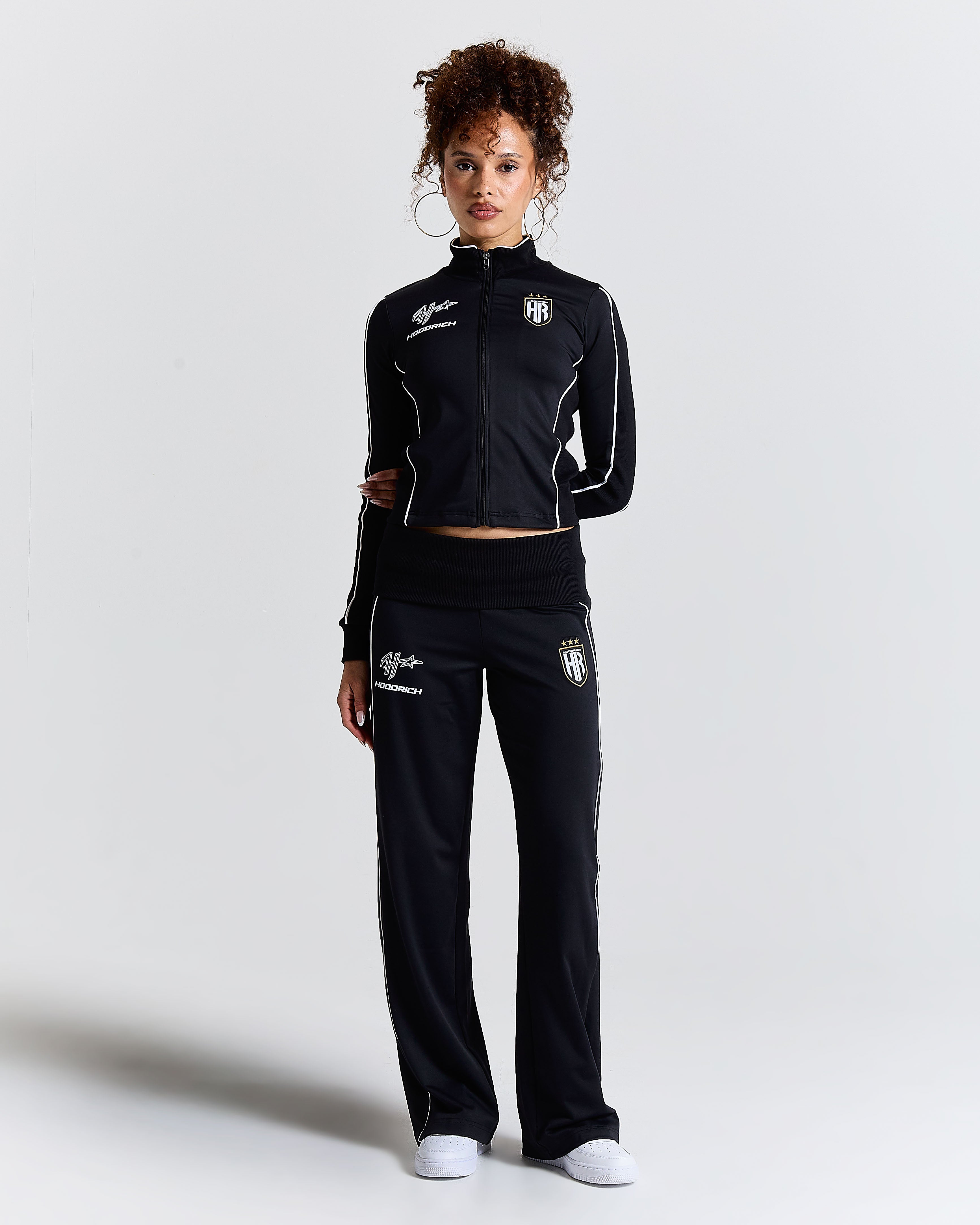Displays a model wearing the Black 'Hoodrich' branded women's Glide Football Full Tracksuit