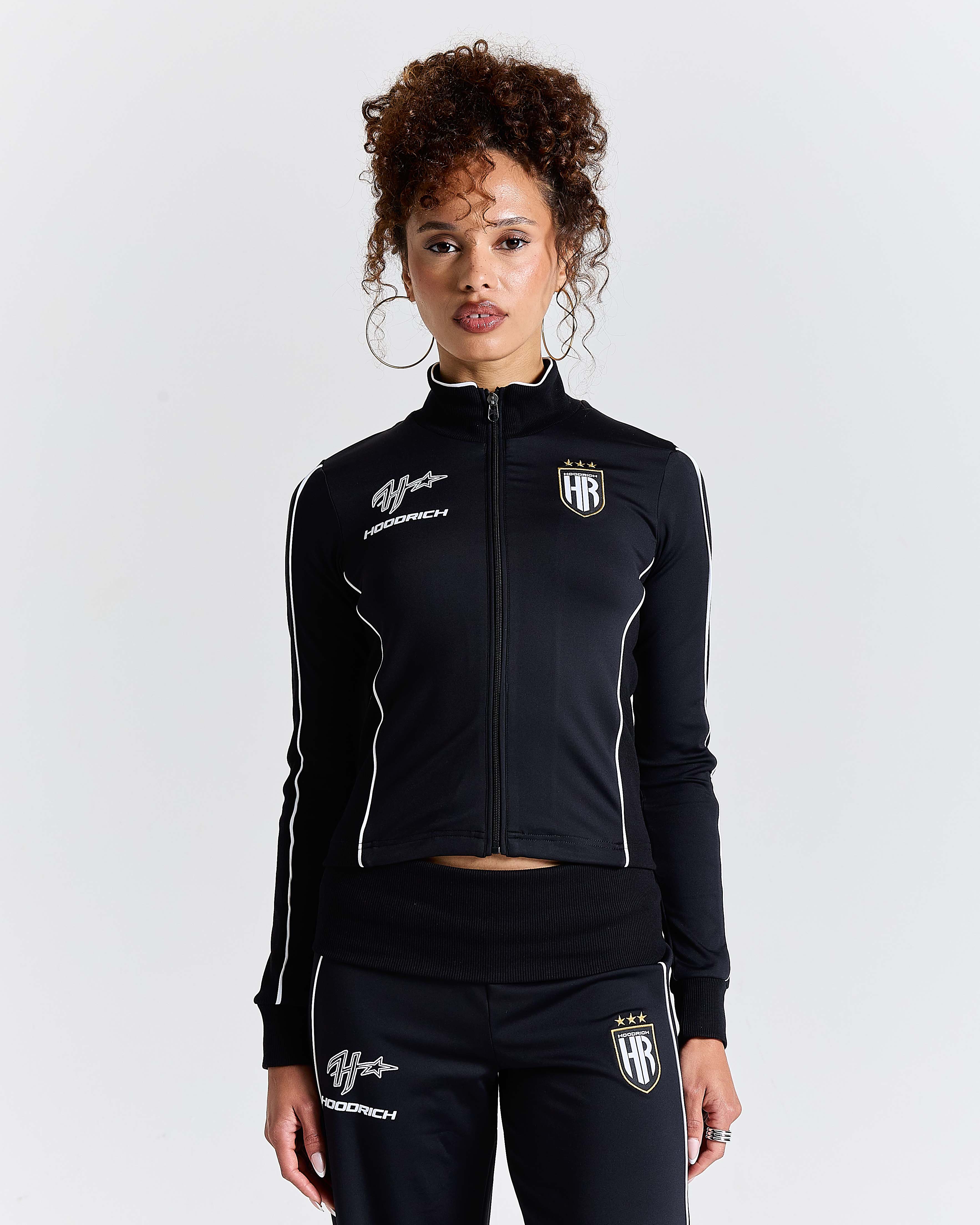 Displays a model wearing the Black 'Hoodrich' branded women's Glide Football Full Tracksuit