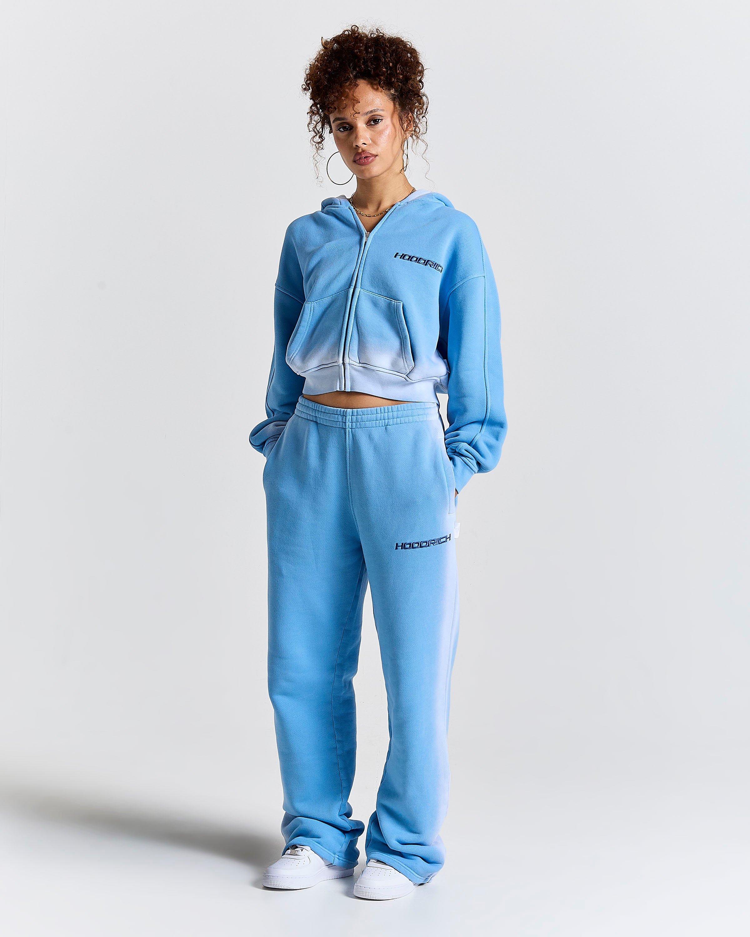 Model wearing a blue ombre zip-up cropped hoodie and matching joggers with Hoodrich logos.