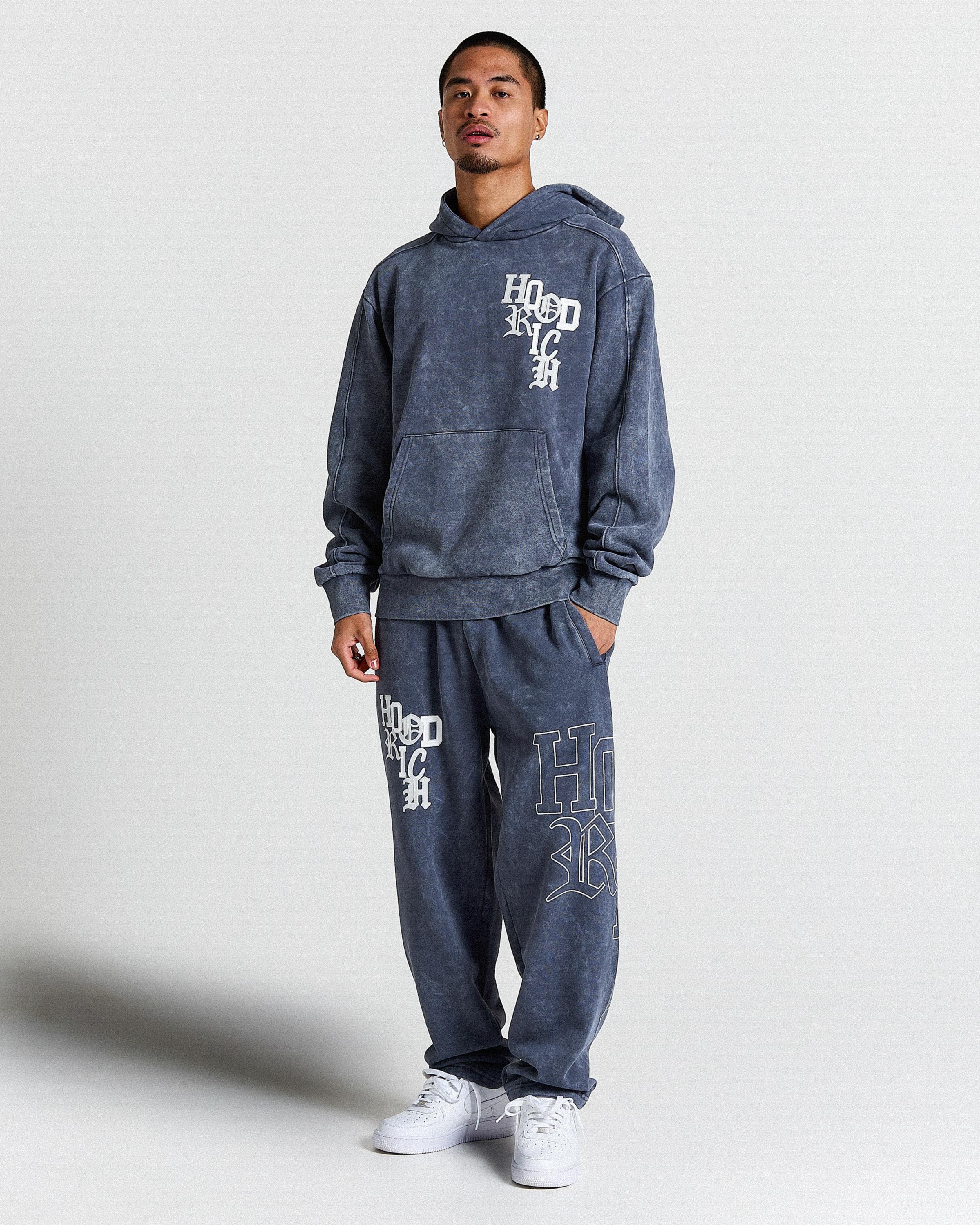 Person wearing a blue hoodie and pants with branding on a white background
