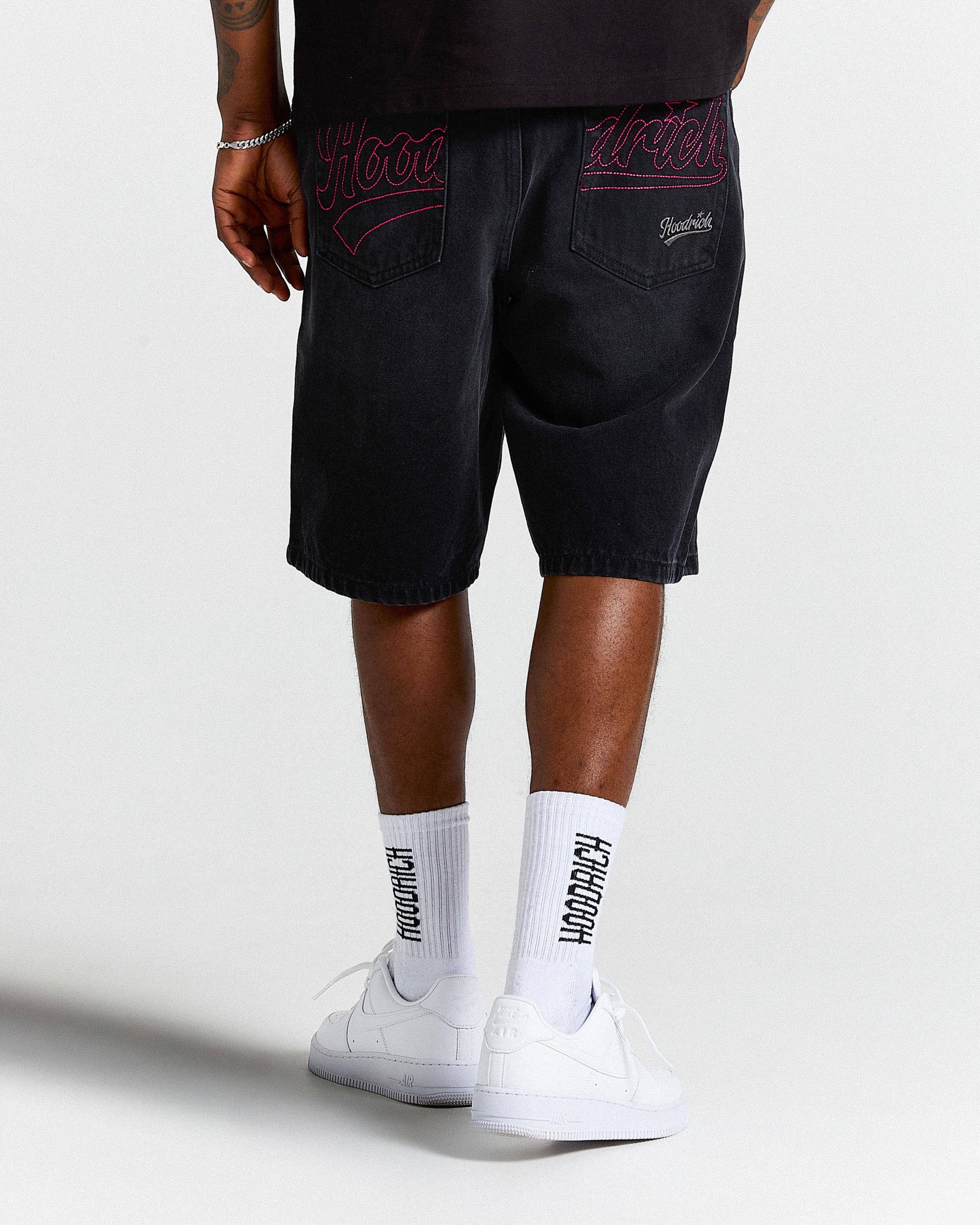 Person wearing black shorts with red embroidery and white socks with text, standing against a white background