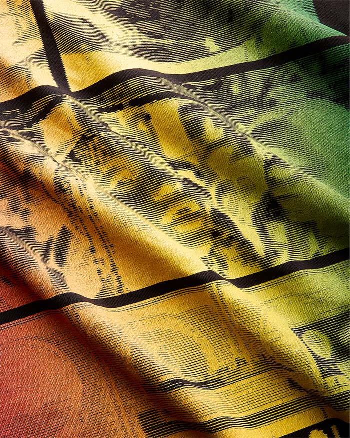 A close-up of a draped fabric with a vintage newspaper print pattern in yellow, green, orange, and black.