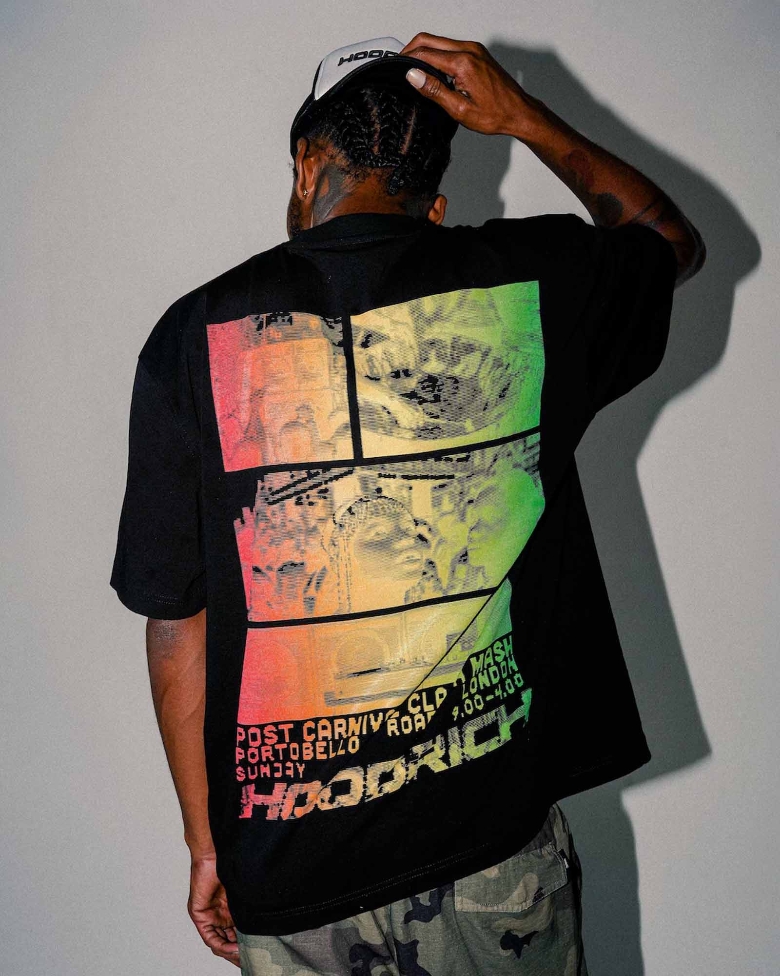 A man viewed from behind wearing a black t-shirt with a large multicolor graphic print on the back, paired with camouflage pants and a white cap.