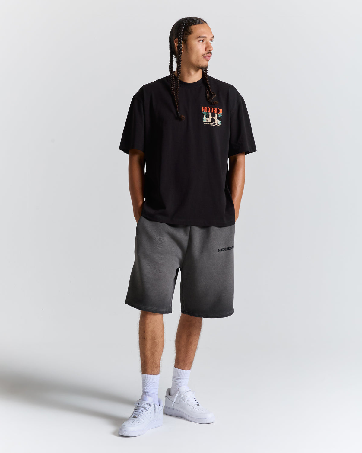 A man modeling a black graphic t-shirt and dark gray heathered shorts against a light gray studio background.