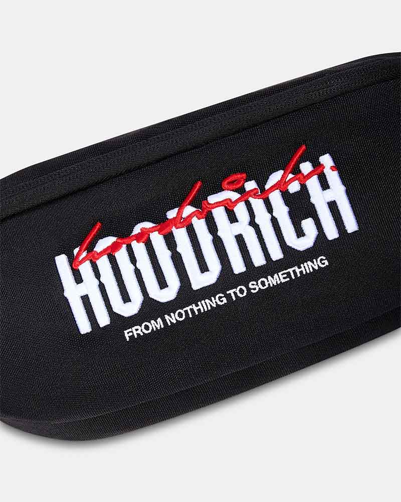 A black cross body bag with a wide, patterned black and red strap. The front features a bold white 'HOODRICH' logo with red graffiti-style lettering above it and smaller white text below reading 'FROM NOTHING TO SOMETHING'.