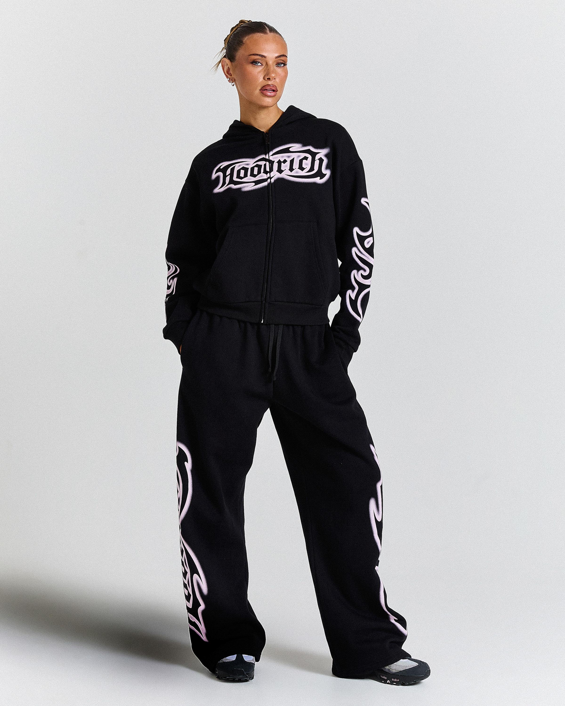 Person wearing a black hoodie and pants with white branding on a light gray background