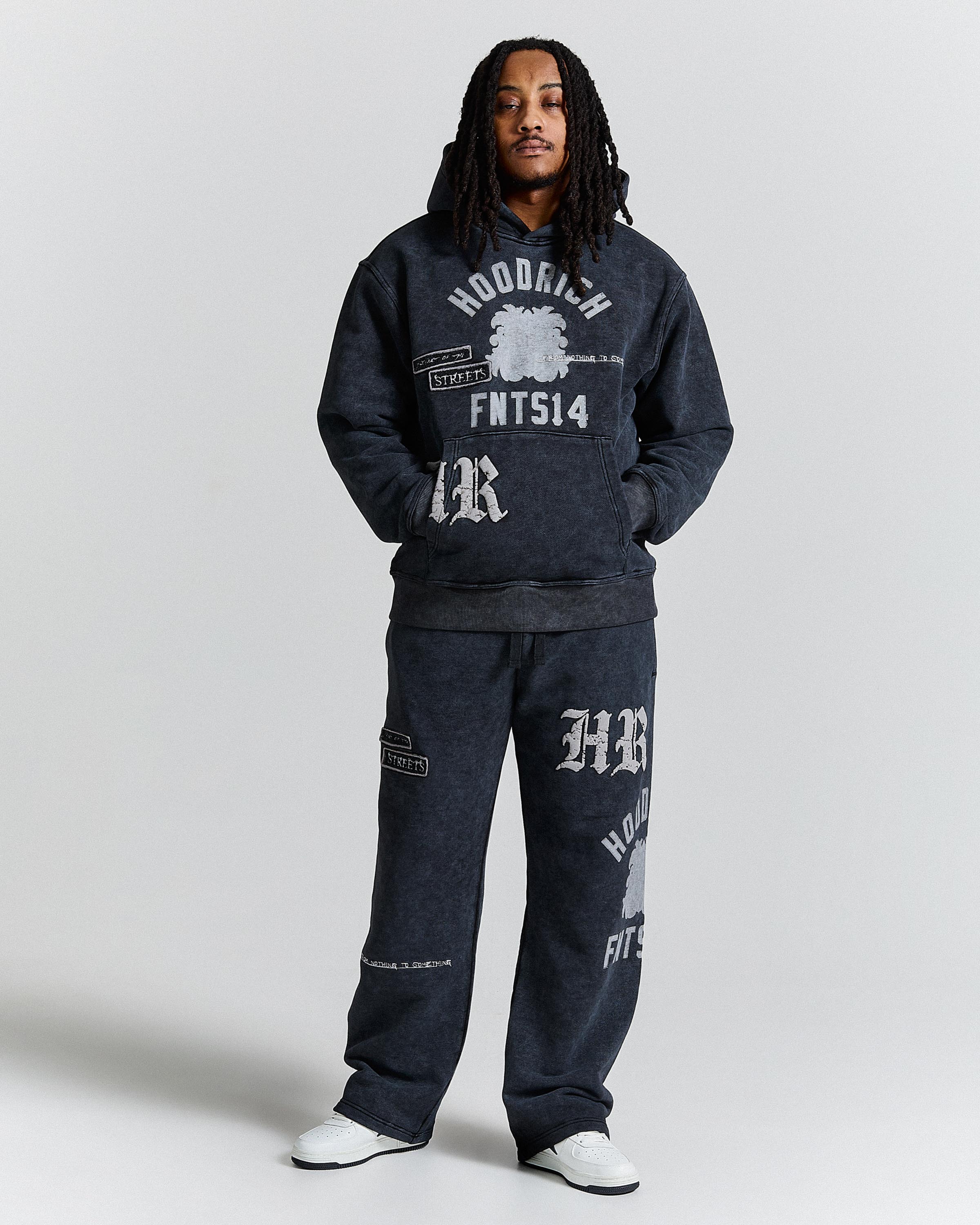 Person wearing a dark gray hoodie and pants with branding on a light gray background
