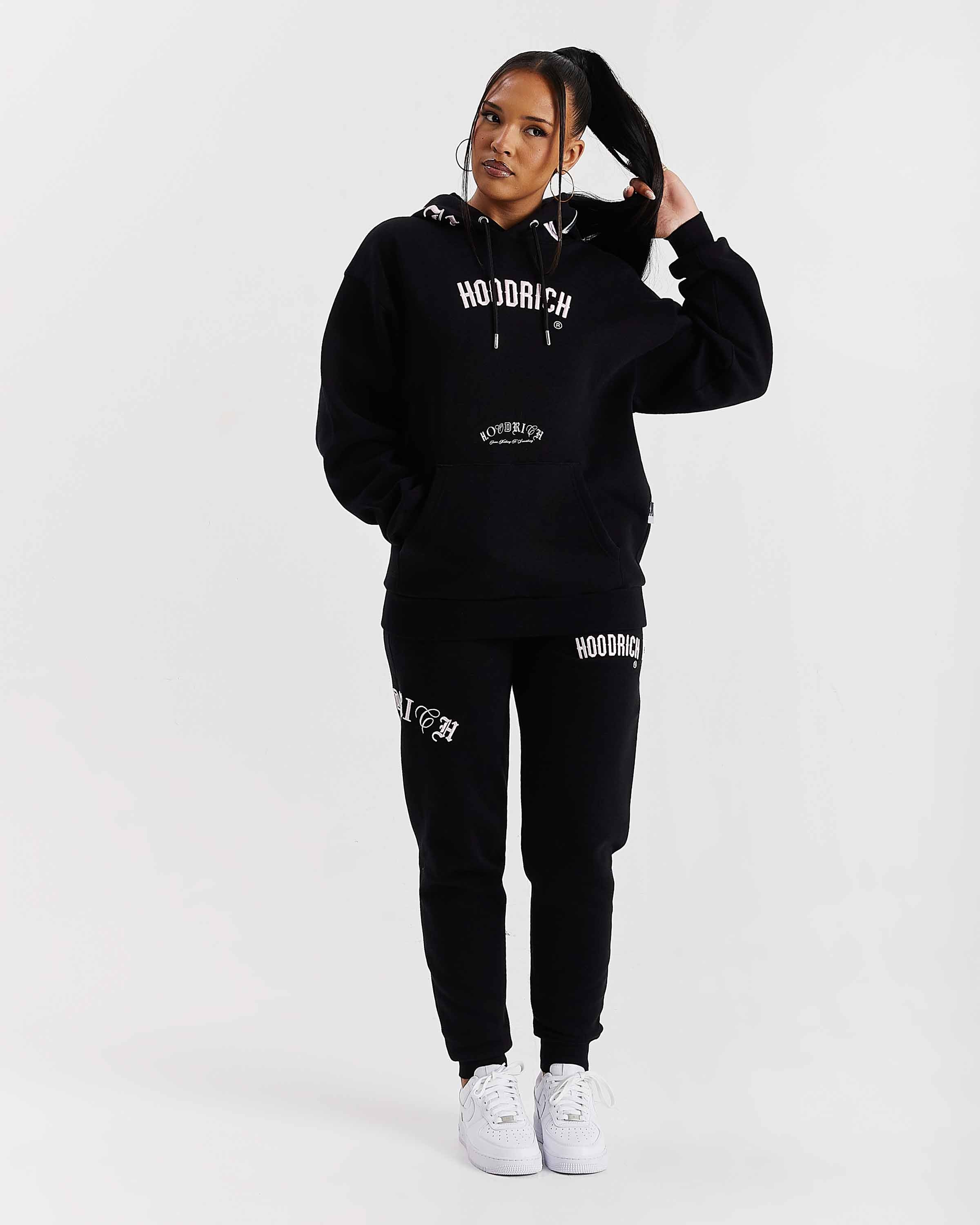 Person wearing a black 'Hoodrich' tracksuit on a white background