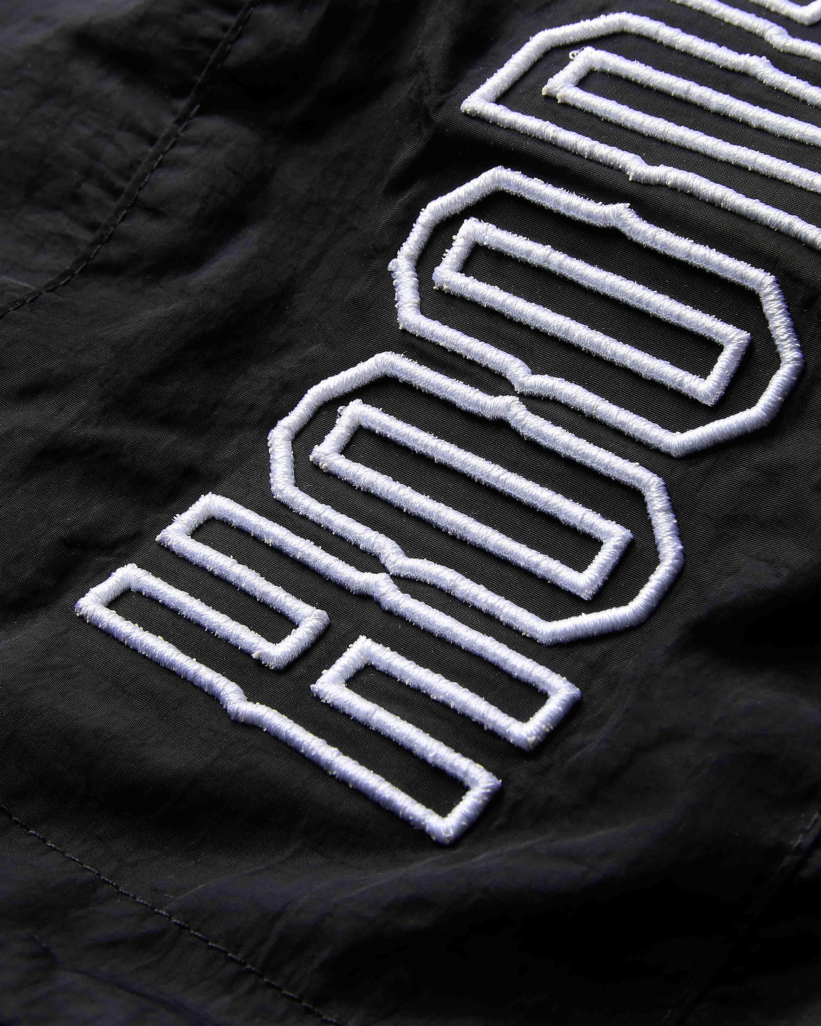 Close-up of a black jacket with white embroidered logo on a dark background