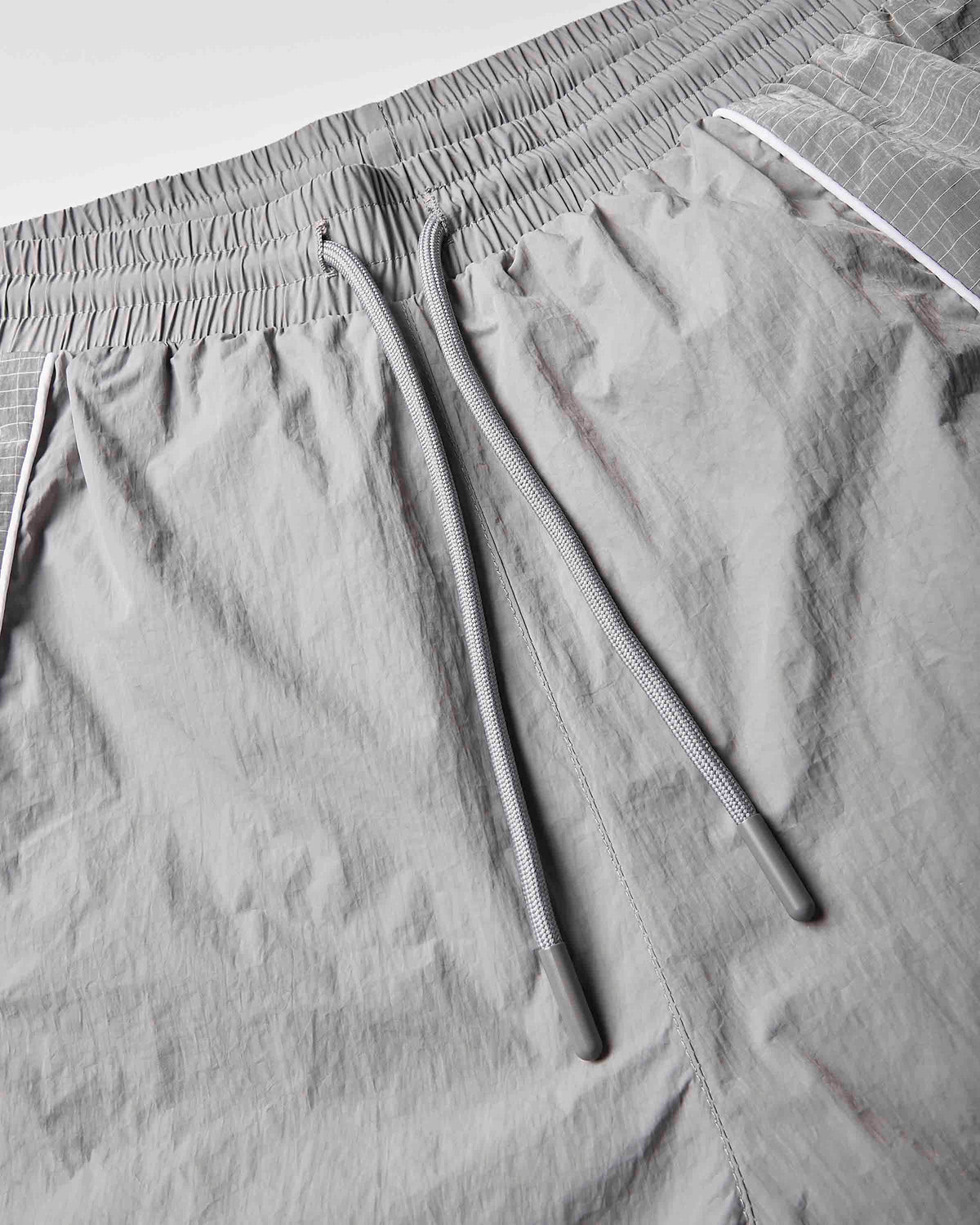 Close-up of light gray athletic shorts showing the elastic waistband, drawstring, and textured fabric.