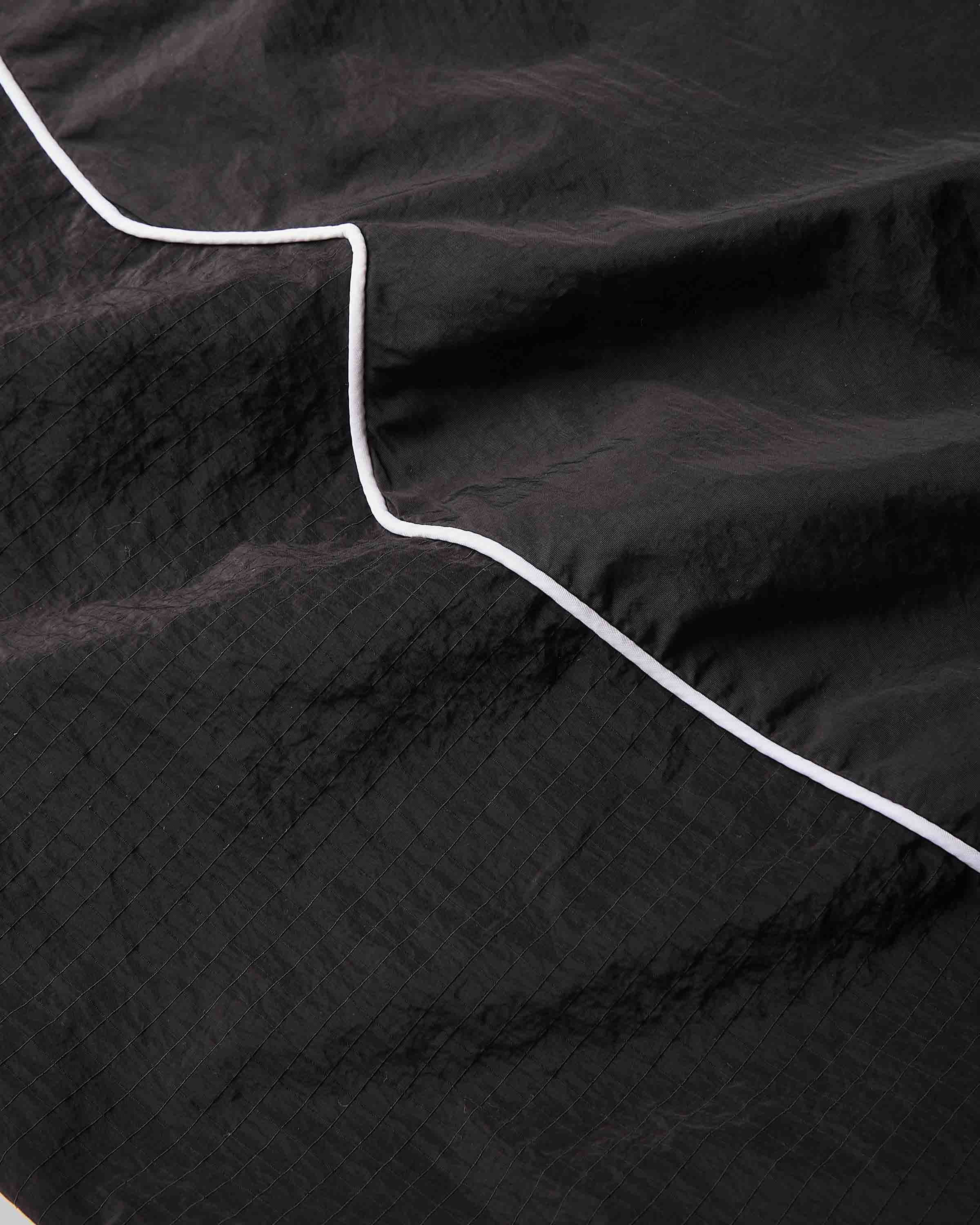 A close-up of a black crinkled fabric with a thin white stitched or printed line running diagonally across it.