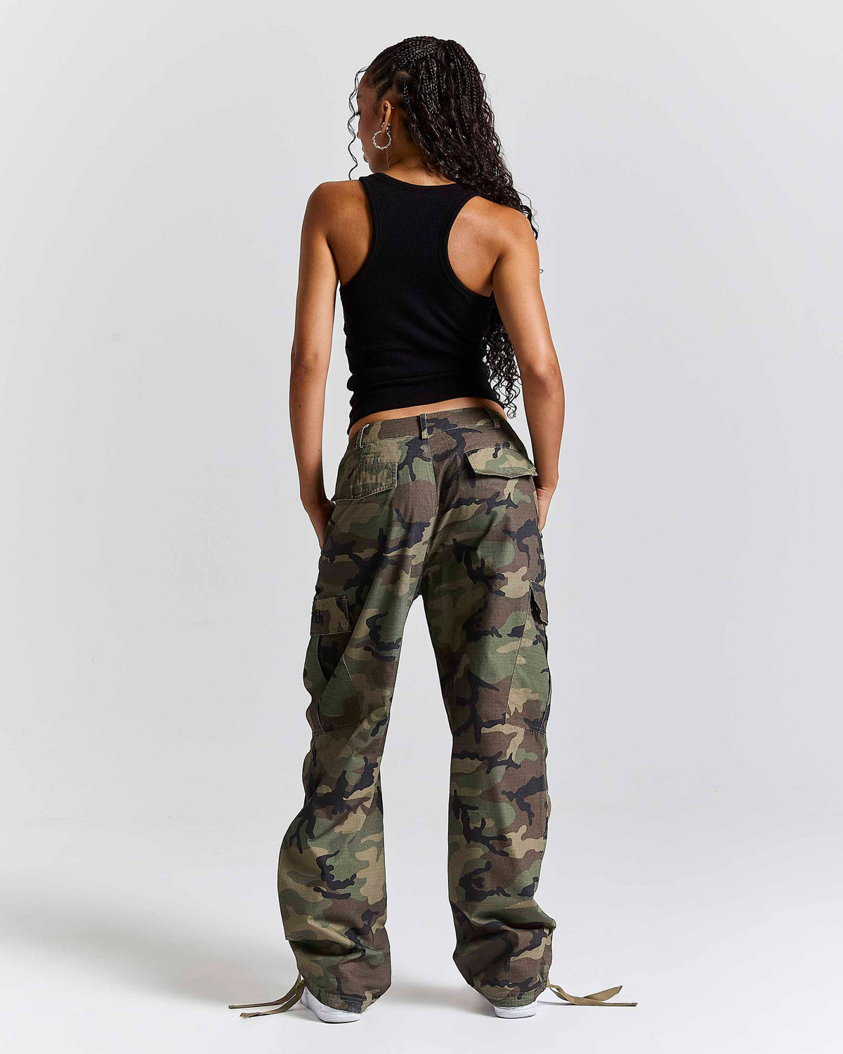 A model shown from the back wearing a black sleeveless top and loose-fit camouflage cargo pants against a light gray studio background.