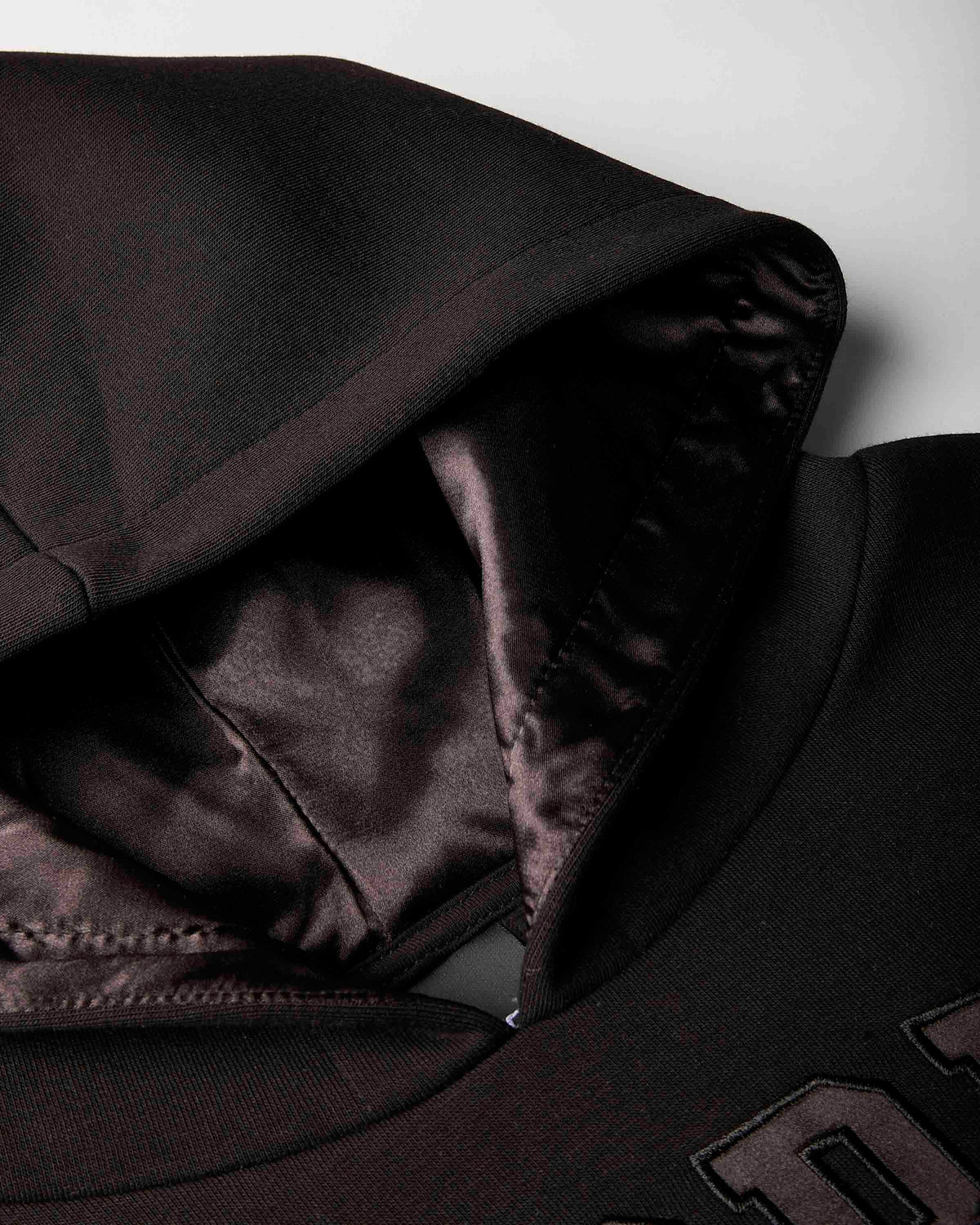 Close-up of a black hooded sweatshirt showing the interior lining of the hood and shoulder area against a light gray background.
