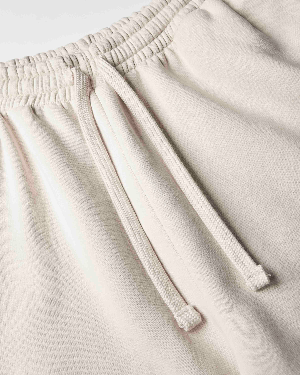 Close-up of a pair of light beige or cream-colored sweatpants, showing the elastic waistband and matching drawstring.