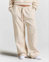 A person wearing cream-colored wide-leg sweatpants with a vertical tonal 'HOODRICH' logo on the left leg, paired with white sneakers against a light gray studio background.