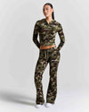 A model wearing a matching camouflage zip-up hoodie and flared sweatpants set, standing against a light gray studio background.