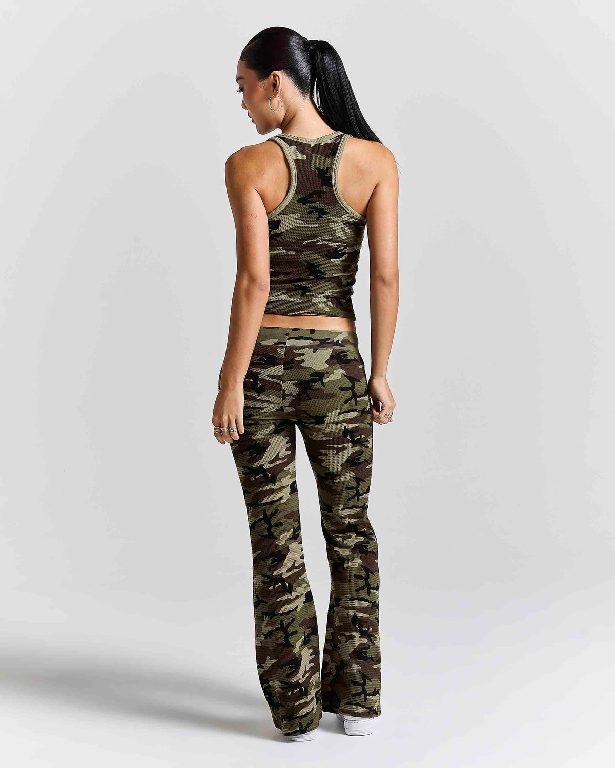 A woman shown from the back wearing a matching camouflage activewear set consisting of a racerback crop top and high-waisted flared pants, photographed against a light gray studio background.