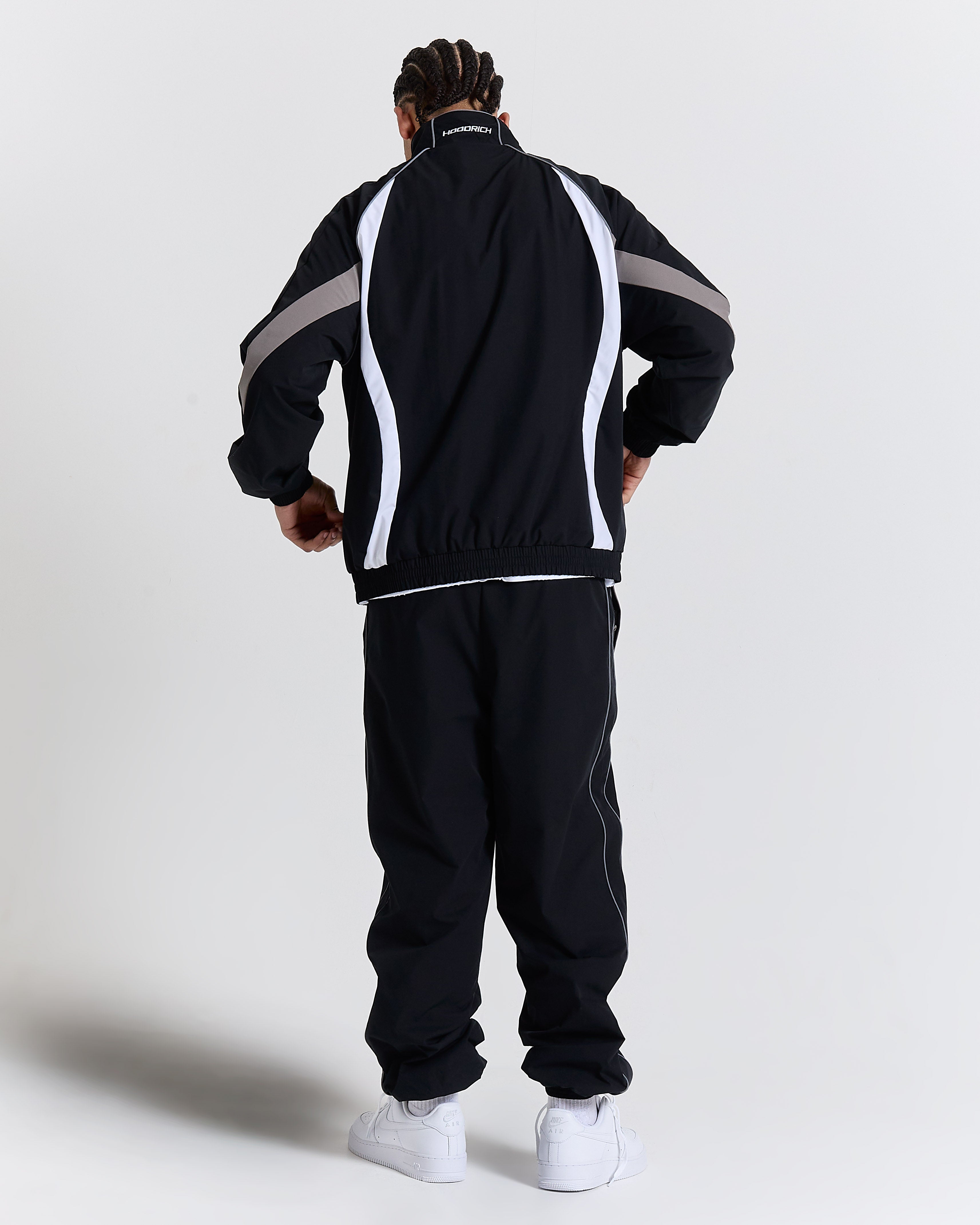Person wearing a black tracksuit with white and gray stripes on a light gray background