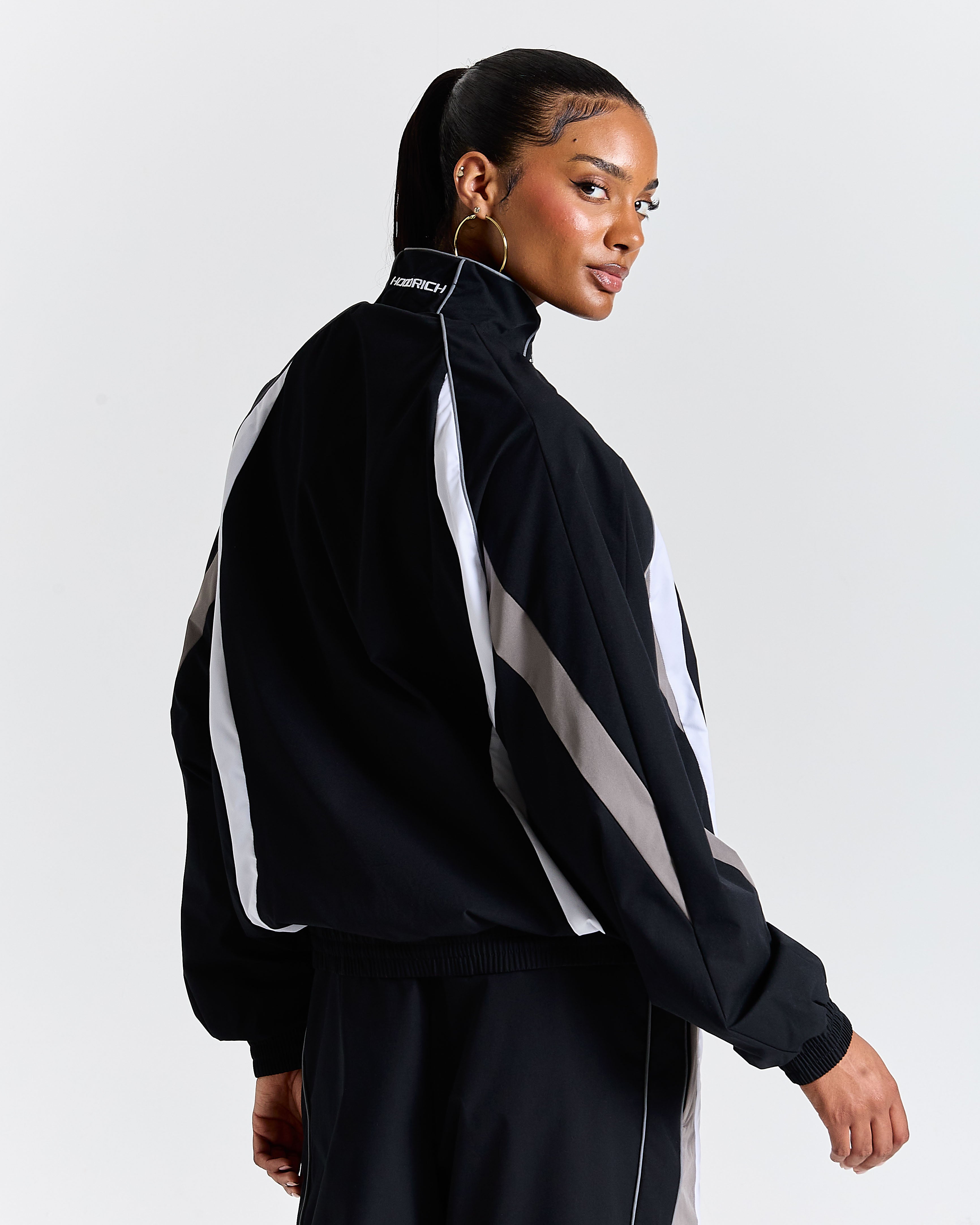 Person wearing a black and white tracksuit with a visible brand logo on a light gray background