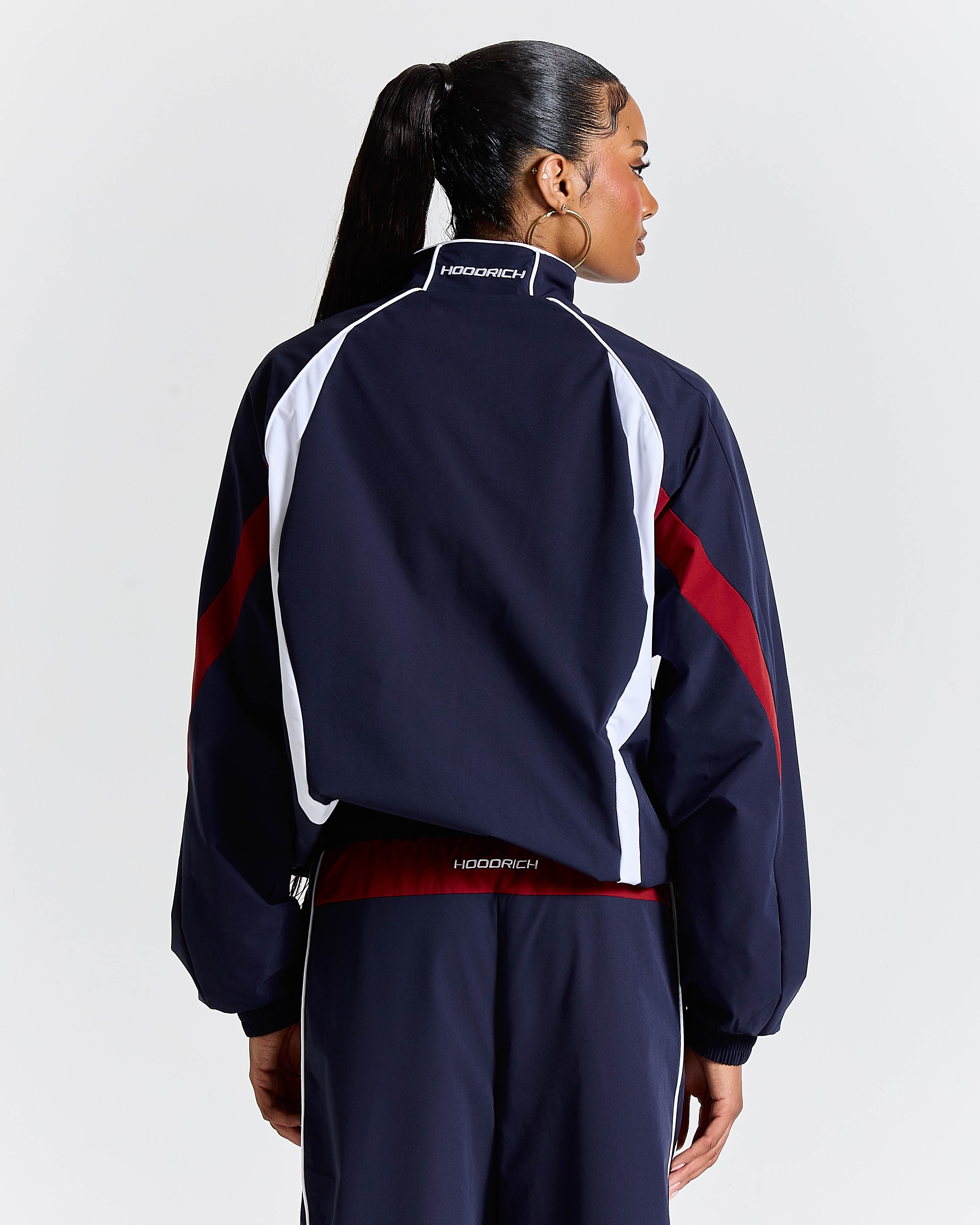 Person wearing a navy tracksuit with red and white accents on a light gray background