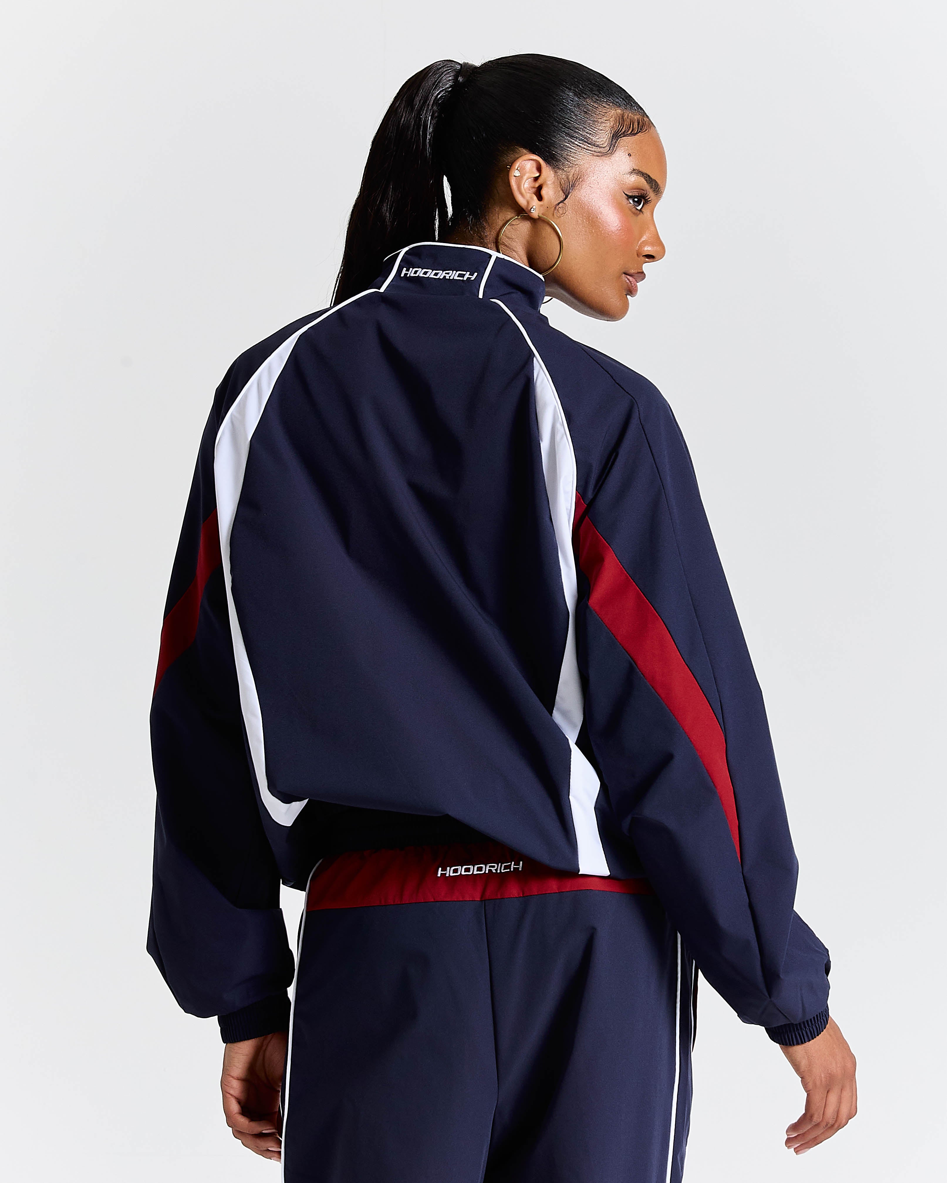 Person wearing a navy tracksuit with red and white accents on a light gray background