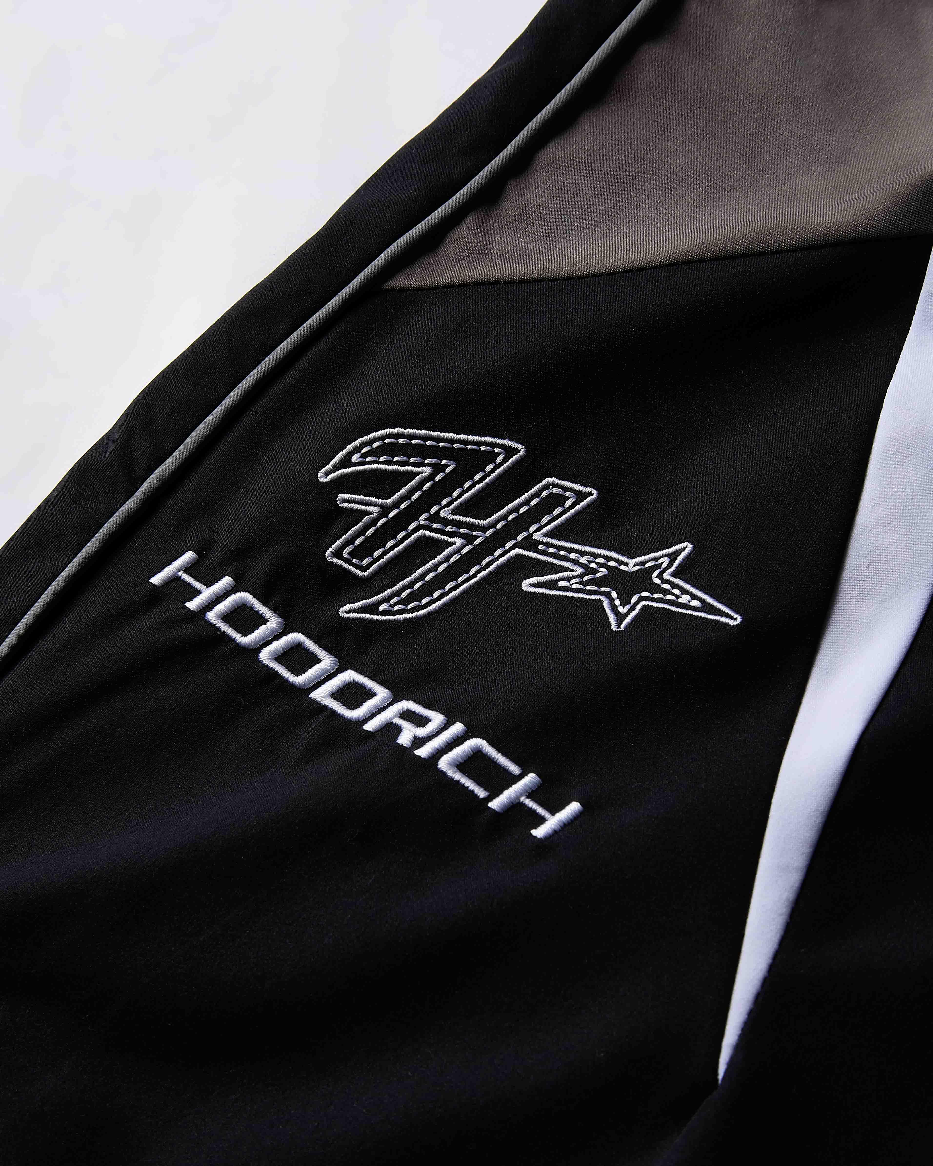 Black jacket with white embroidered logo and text on a light gray background
