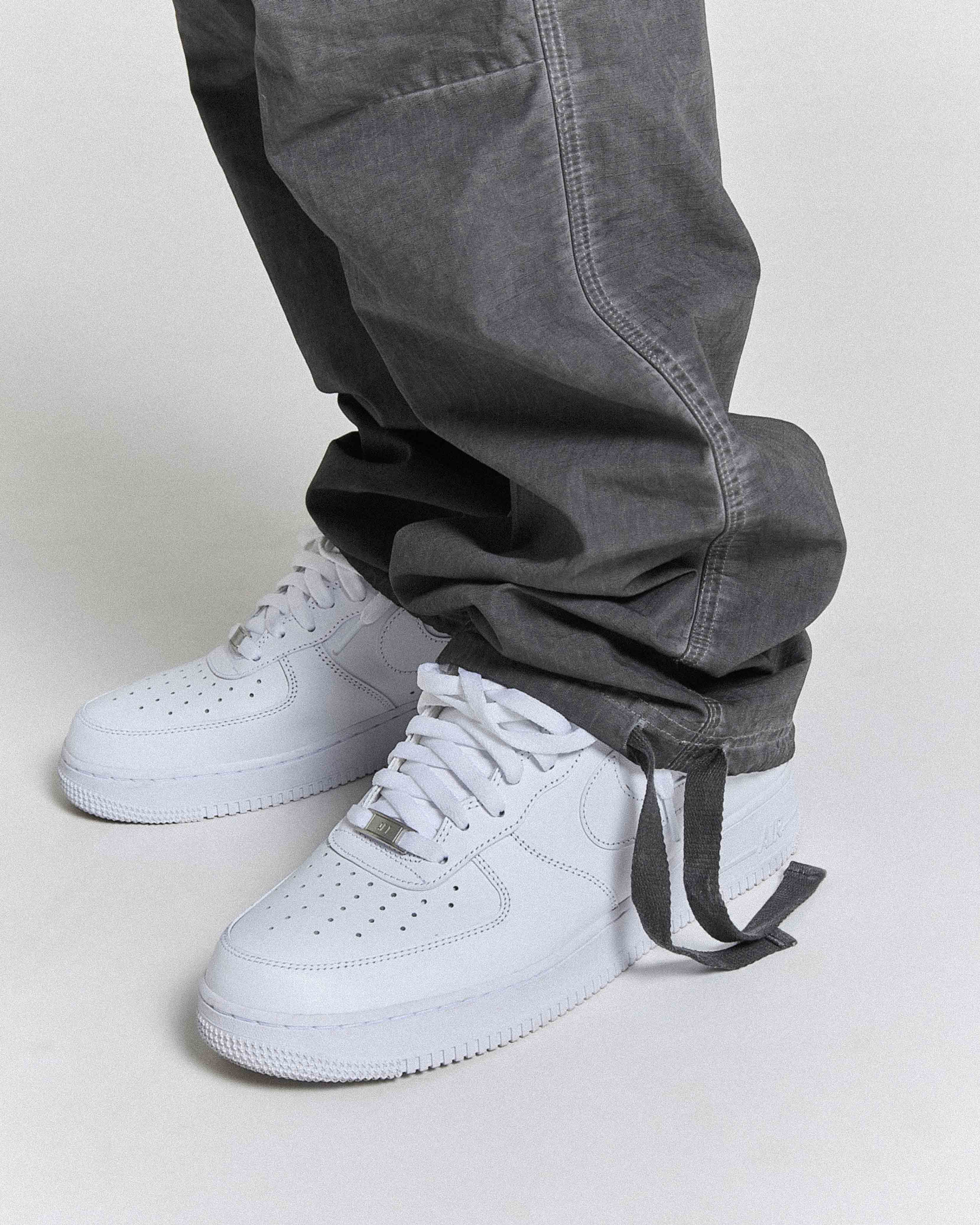 White sneakers with a gray pant cuff on a light gray background