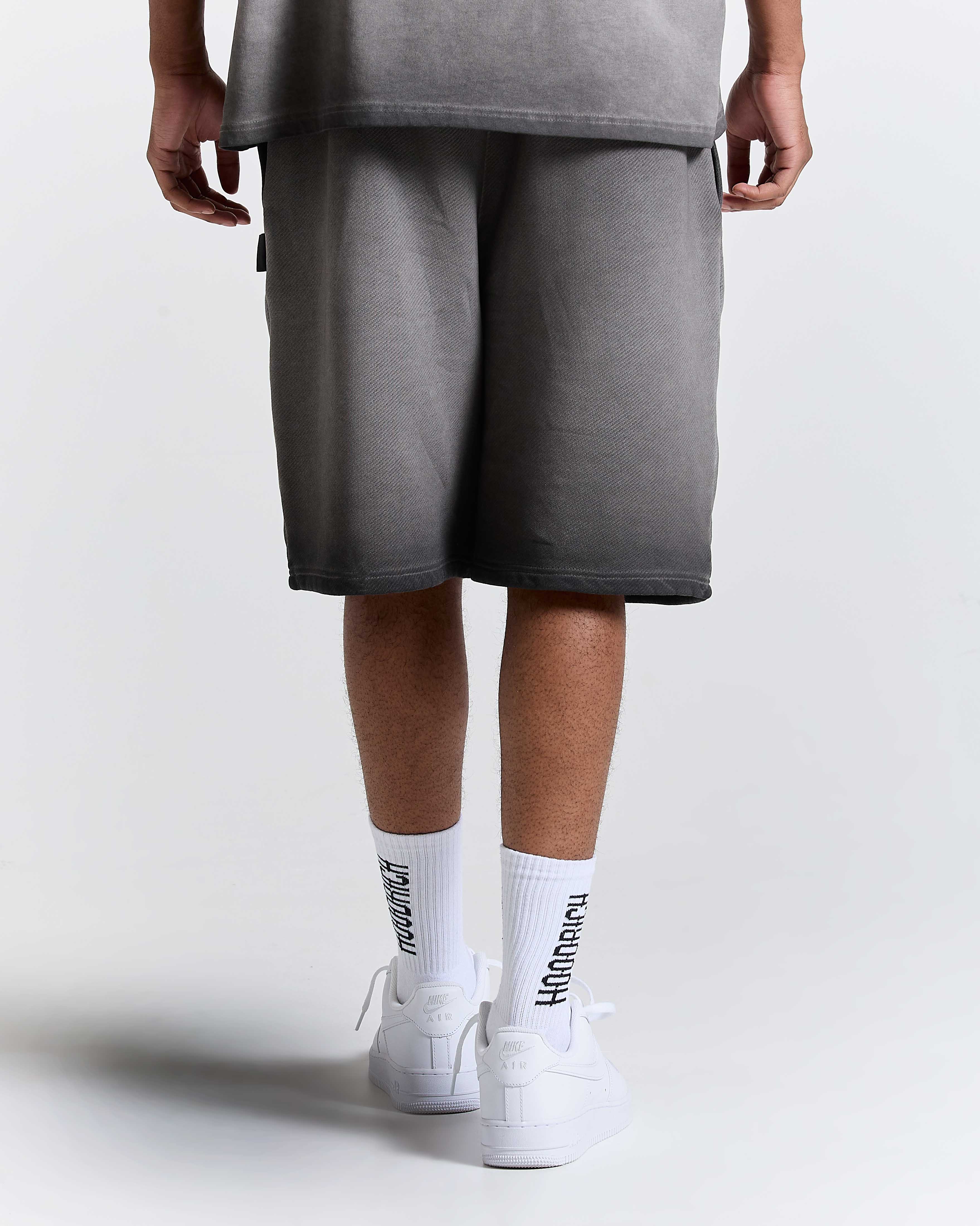 Model seen from behind wearing oversized black oil wash shorts, white socks, and white trainers.
