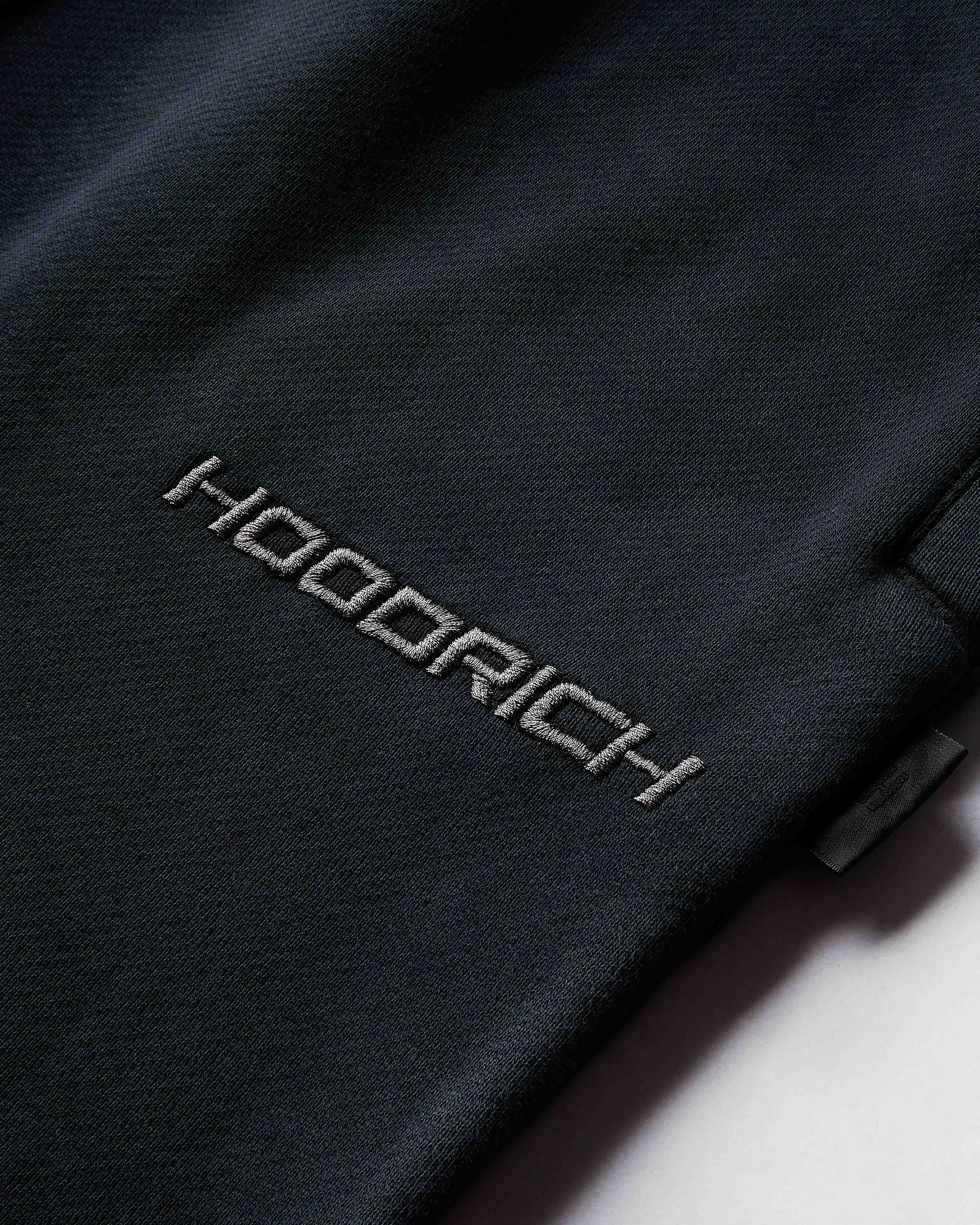 Close-up of a black jacket with 'Hoodrich' branding on a white background