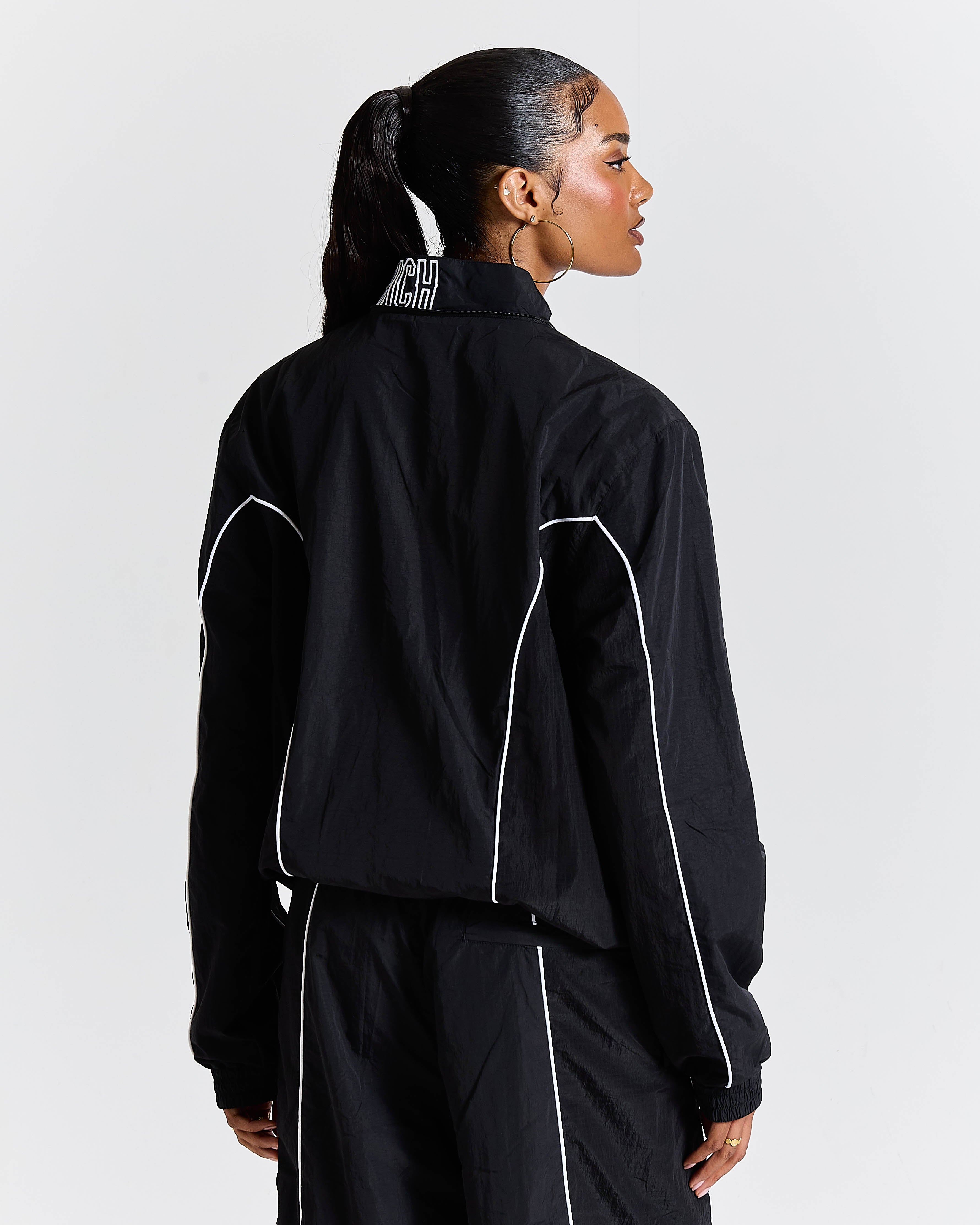 Person wearing a black tracksuit with white piping on a light gray background