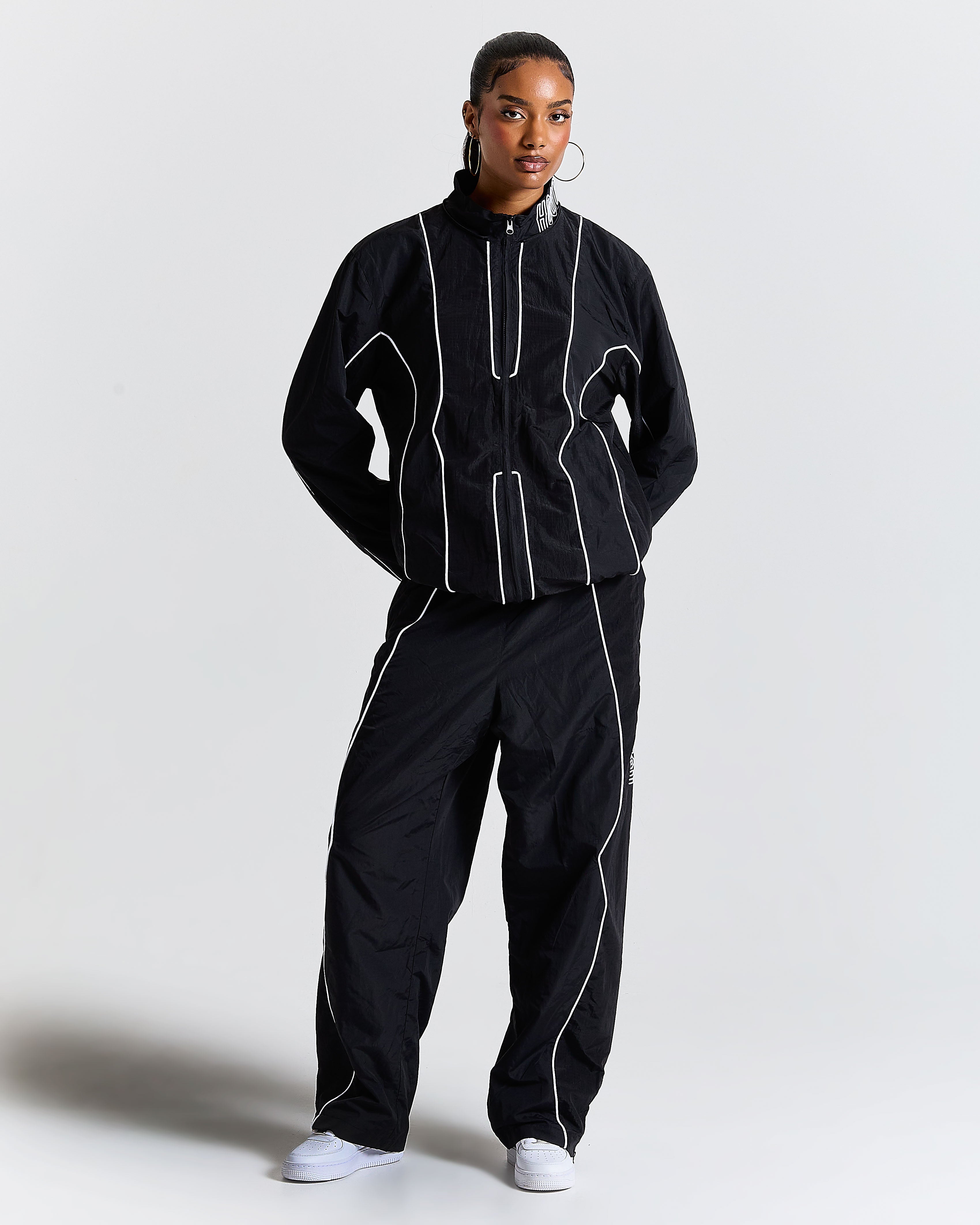 Person wearing a black tracksuit with white accents on a plain background