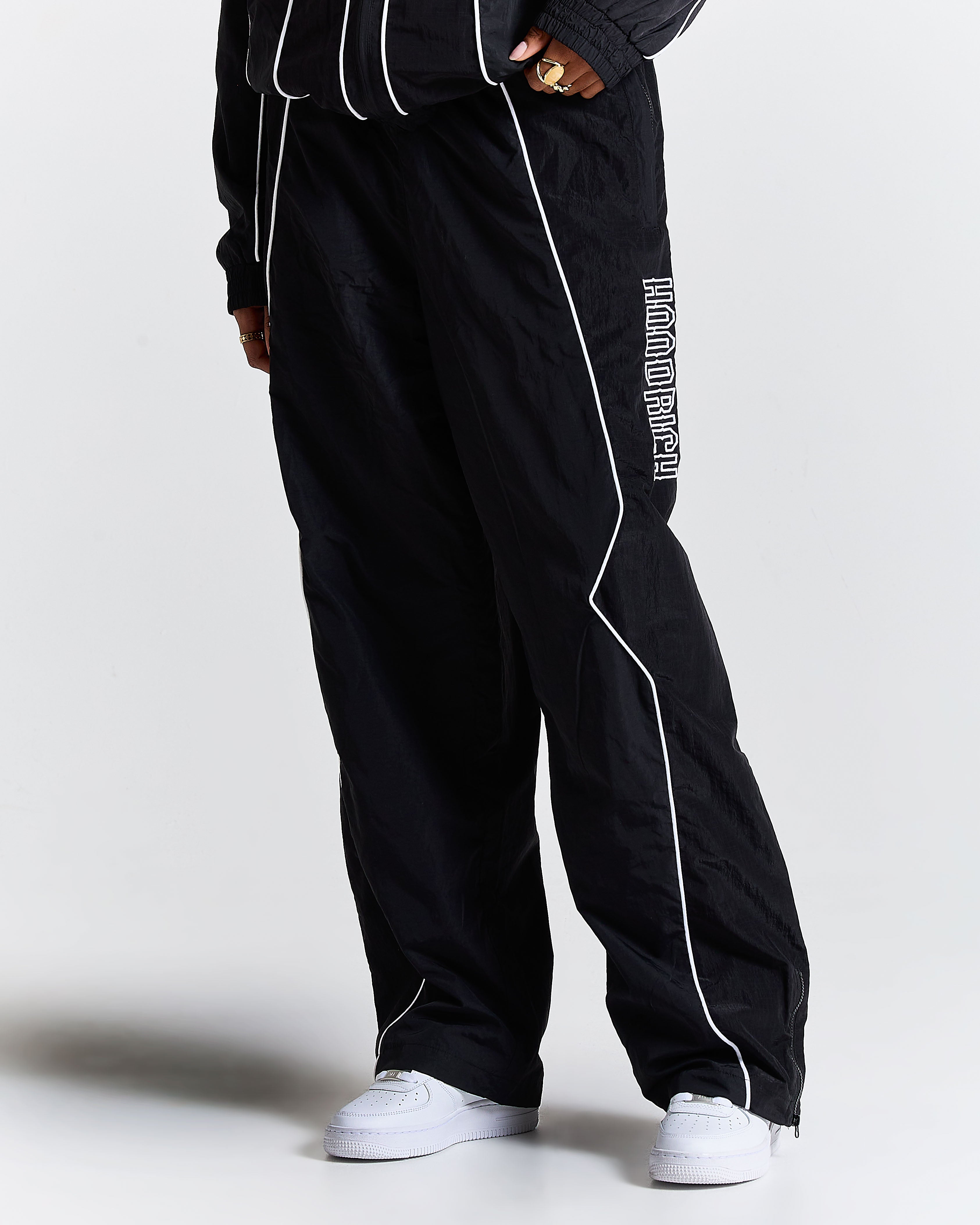 Black track pants with white piping and text on a plain background