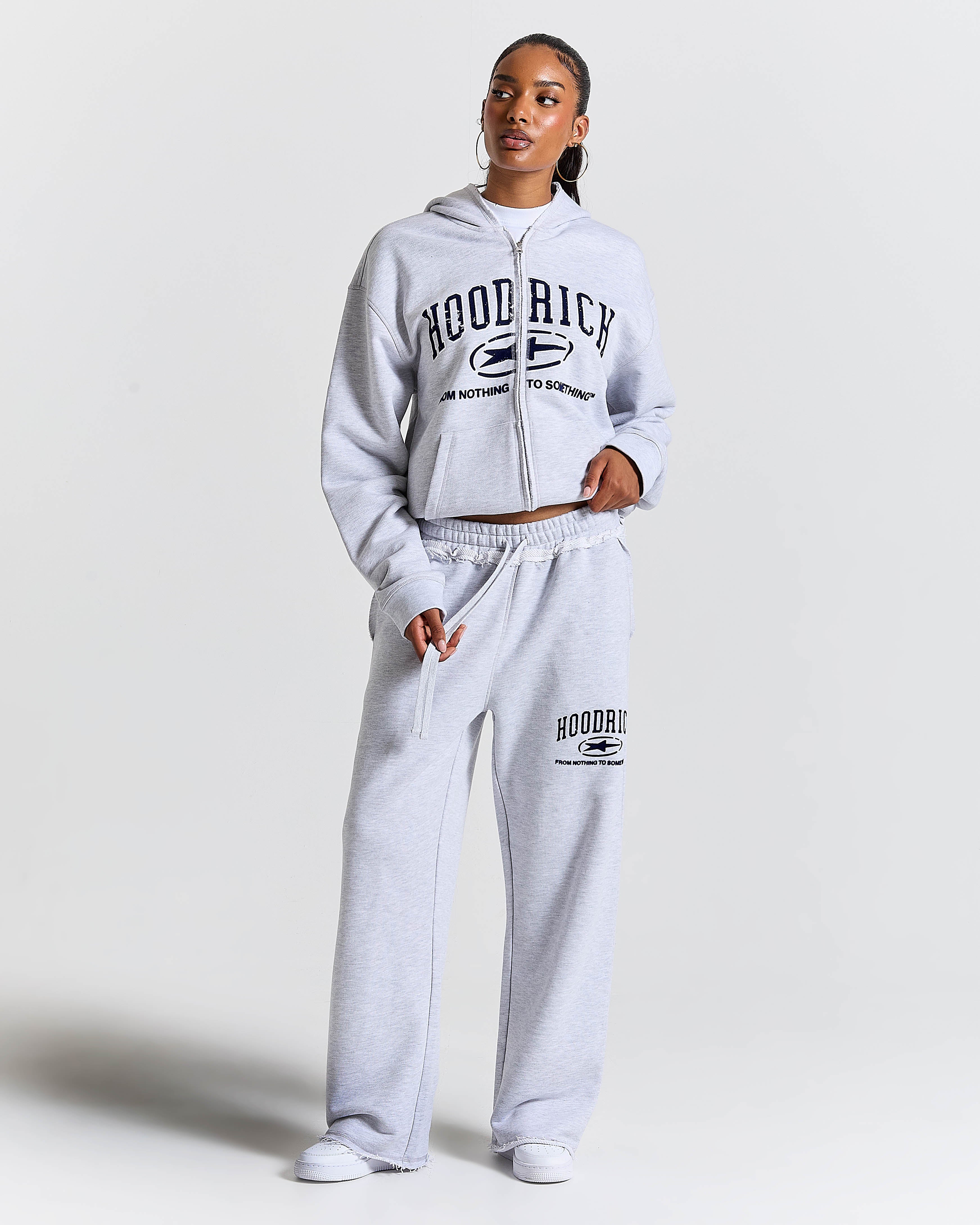 Person wearing a gray 'Hood Rich' tracksuit on a white background