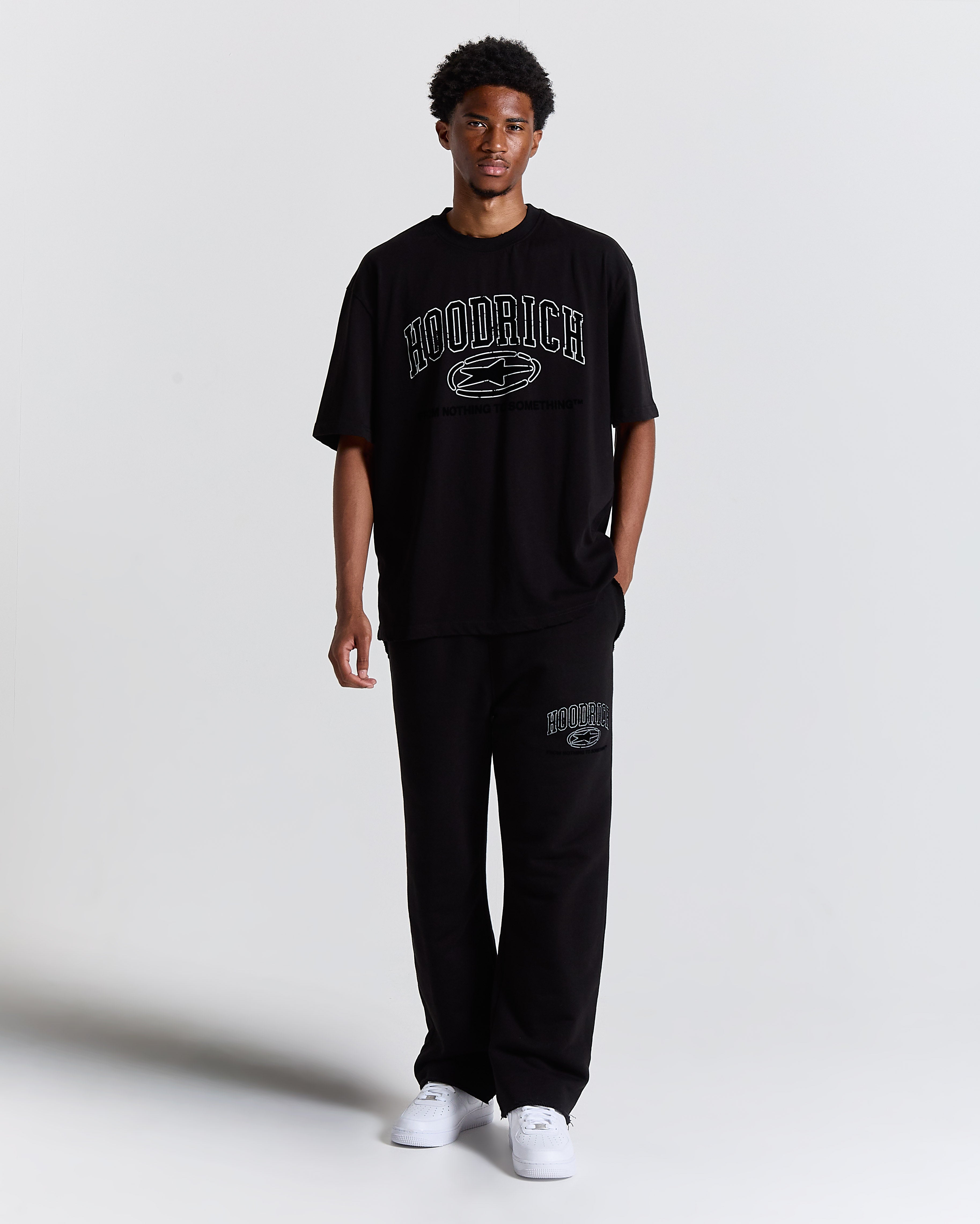 Person wearing a black 'Hoodrich' t-shirt and pants on a white background