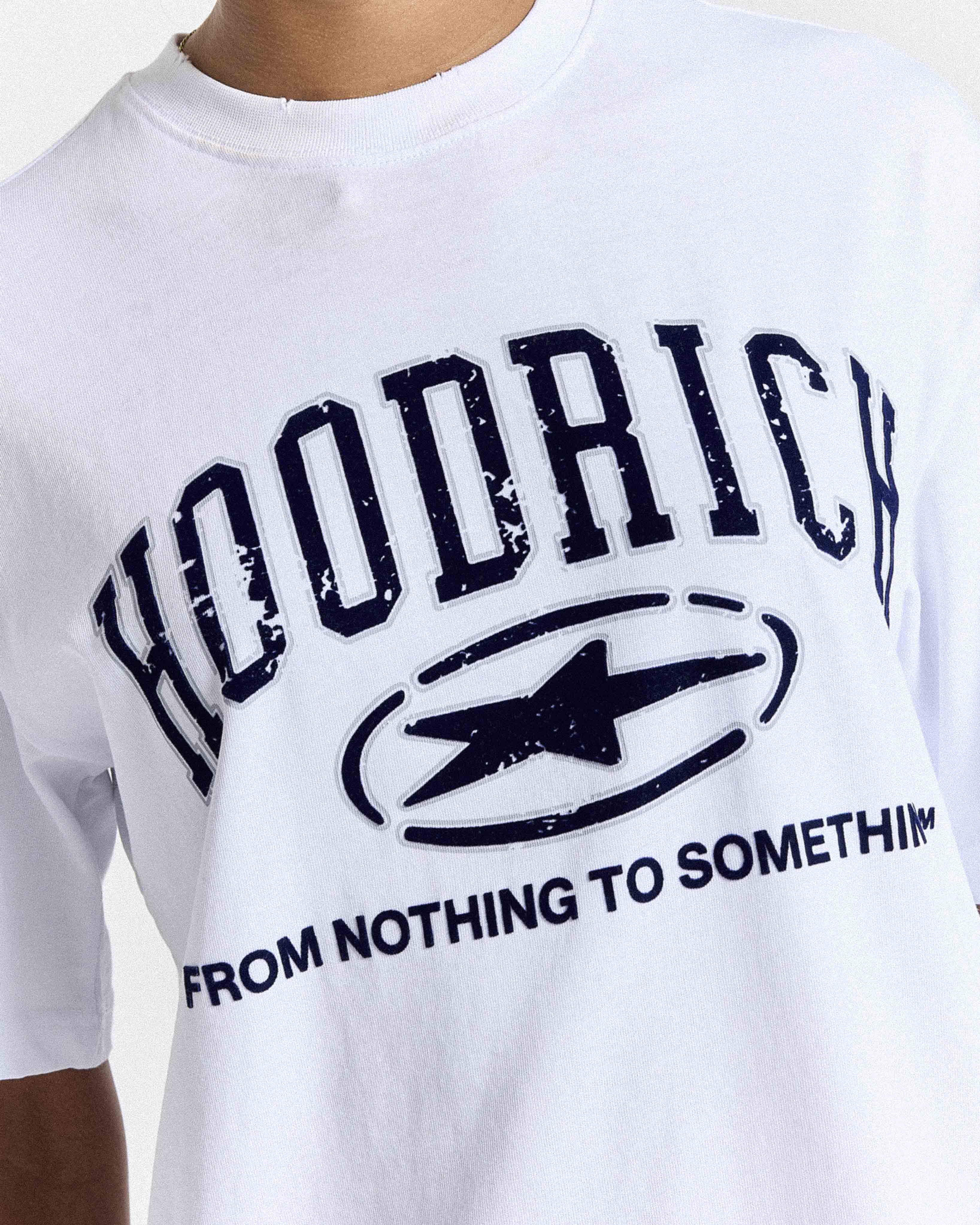 White crewneck t-shirt featuring a distressed navy blue graphic print with the text 'HOODRICH' and 'FROM NOTHING TO SOMETHING' surrounding a star logo.