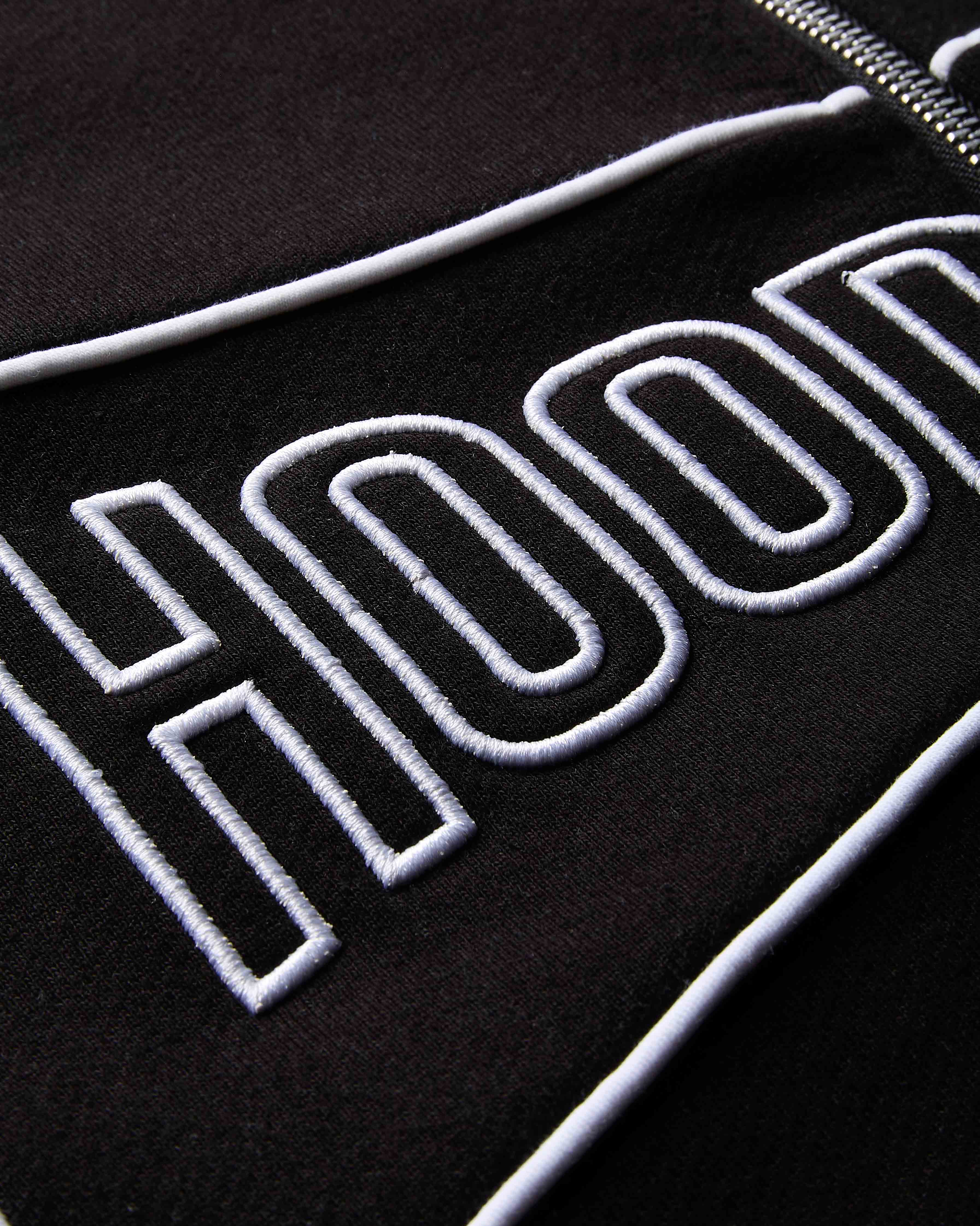 Close-up of a black jacket with 'HOOD' embroidered in white on a dark background